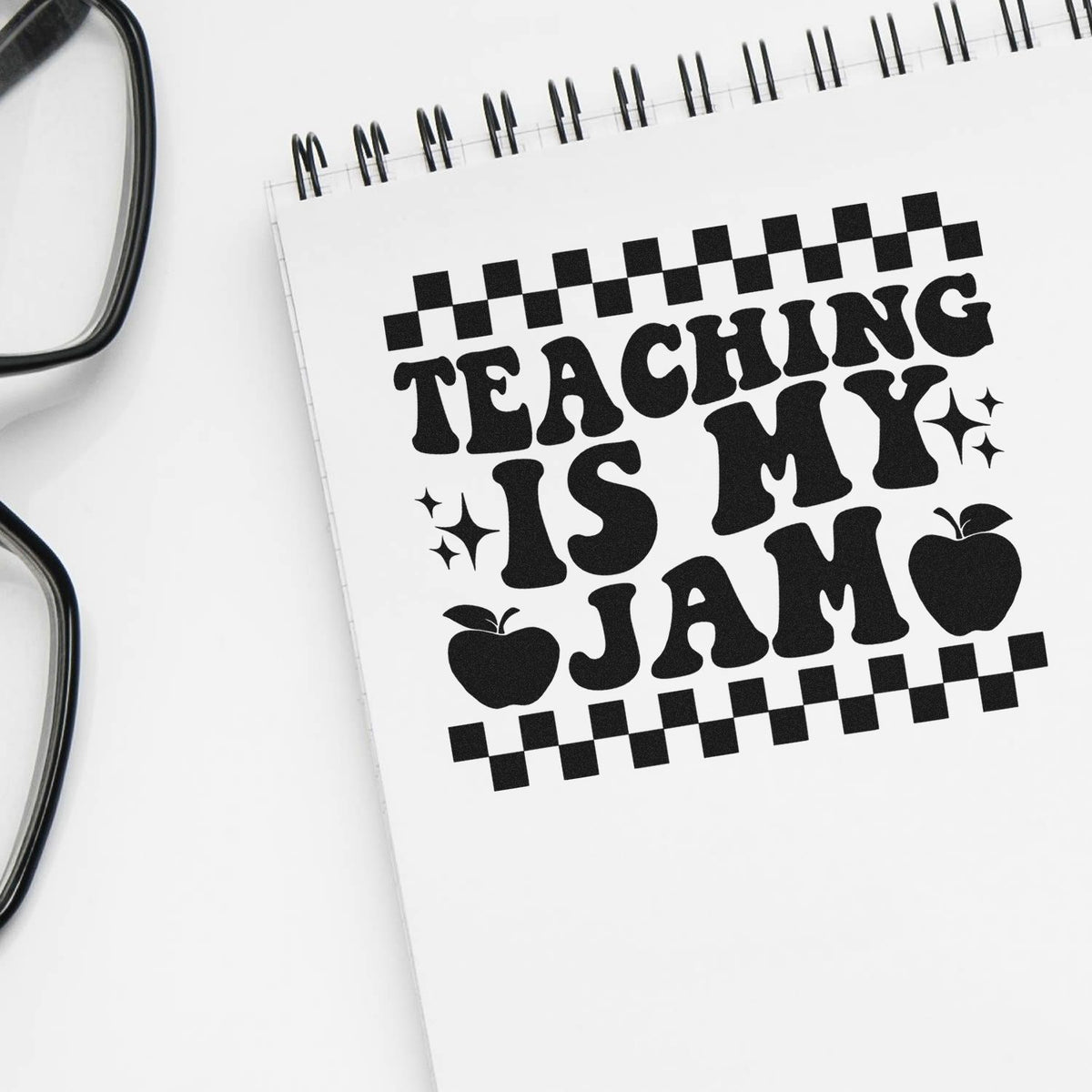 Teacher rubber stamp design reading Teaching Is My Jam on a spiral notebook with apples and checker accents.