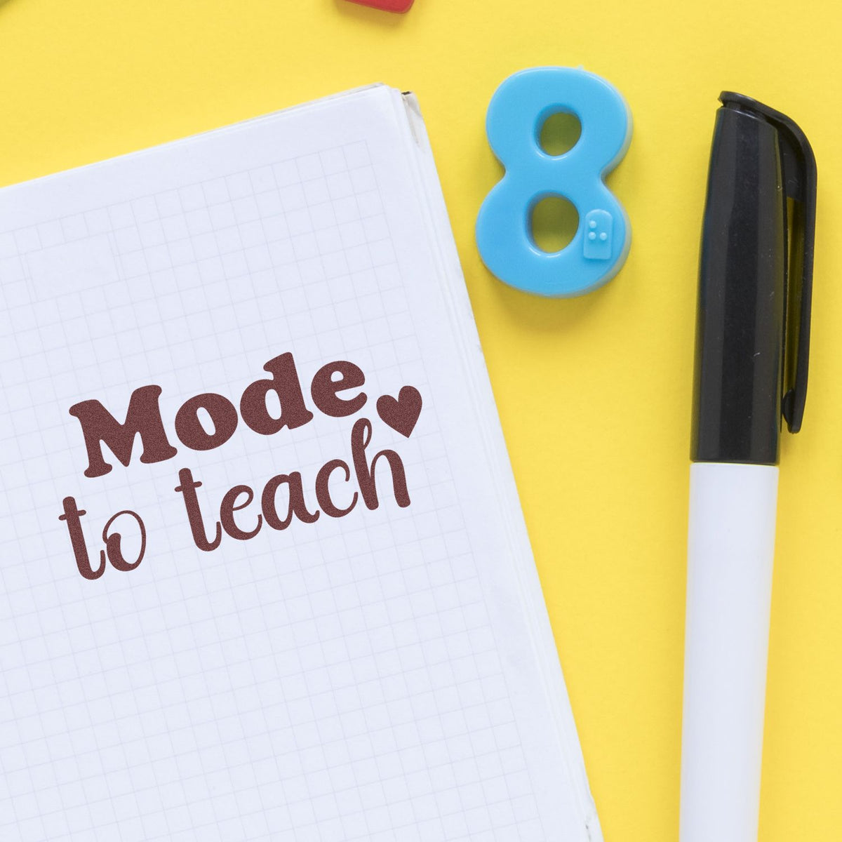 Educational rubber stamp saying Mode to teach beside notebook and pen on yellow background.