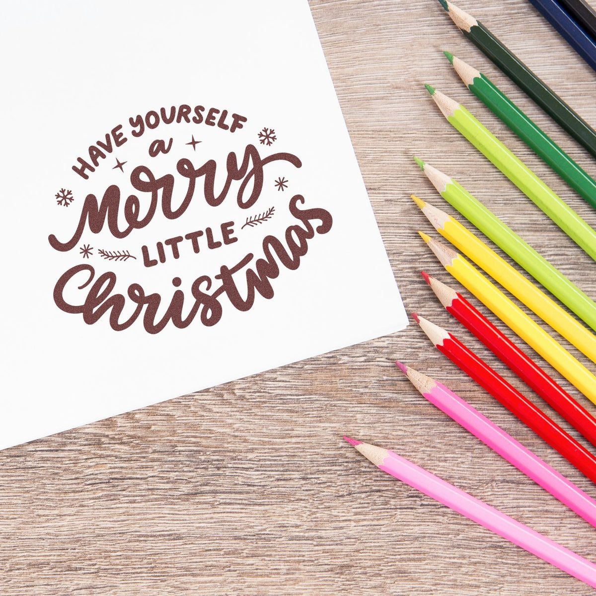 Christmas rubber stamp design reading Have Yourself a Merry Little Christmas on paper, with colorful pencils for holiday card making.