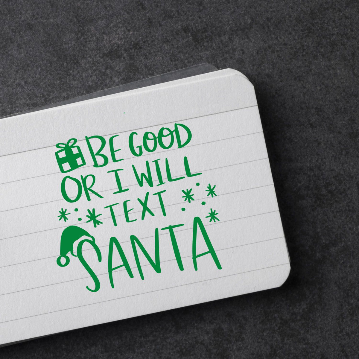 Christmas rubber stamp impression reading Be good or I will text Santa on notebook paper with gift and Santa hat icons.