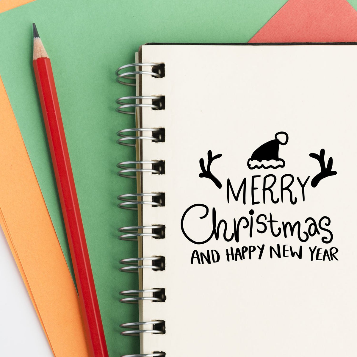 Holiday rubber stamp design reading Merry Christmas and Happy New Year in a spiral notebook with pencil and colorful paper.