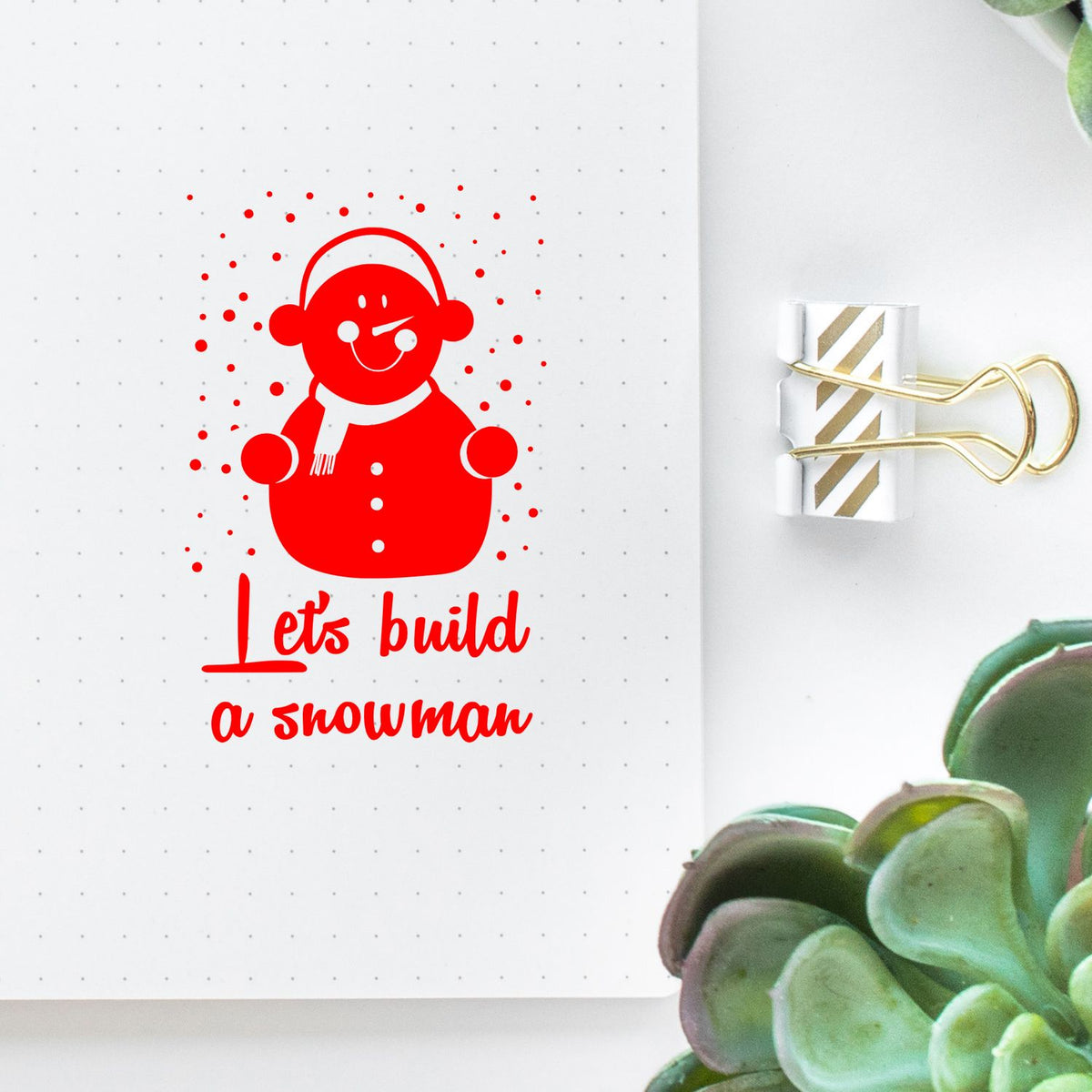 Red snowman rubber stamp design with Lets build a snowman text on a planner page, perfect for holiday crafting.