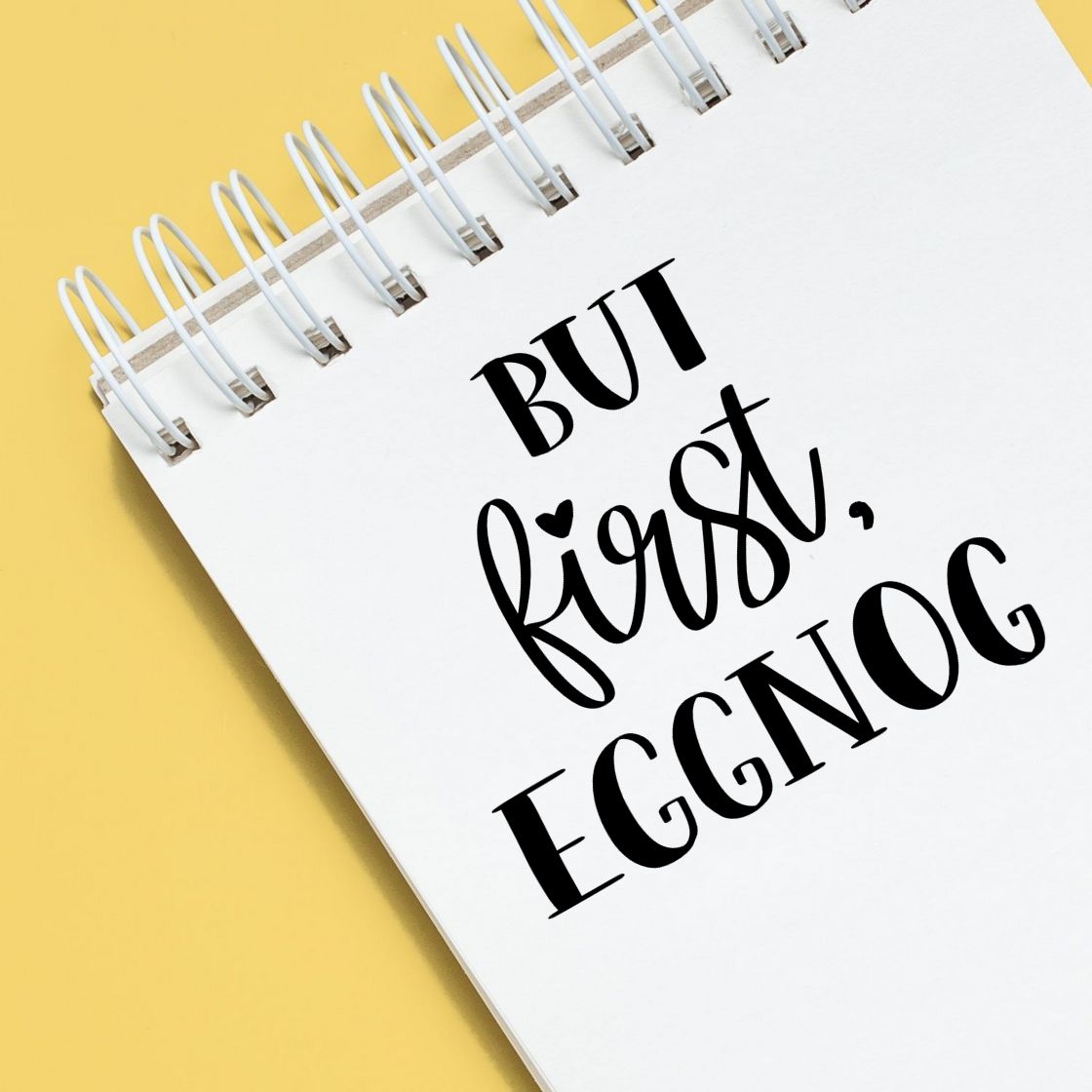 Custom rubber stamp design with But first, eggnog on a spiral notebook, perfect for holiday crafts and gift packaging.