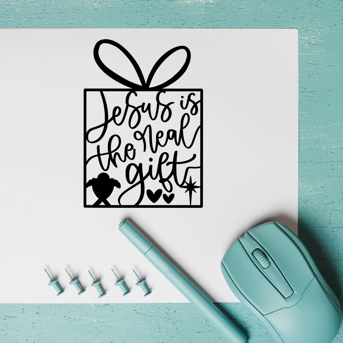 Jesus is the real gift Christian rubber stamp design with gift box bow, shown with stamping tools and craft supplies.