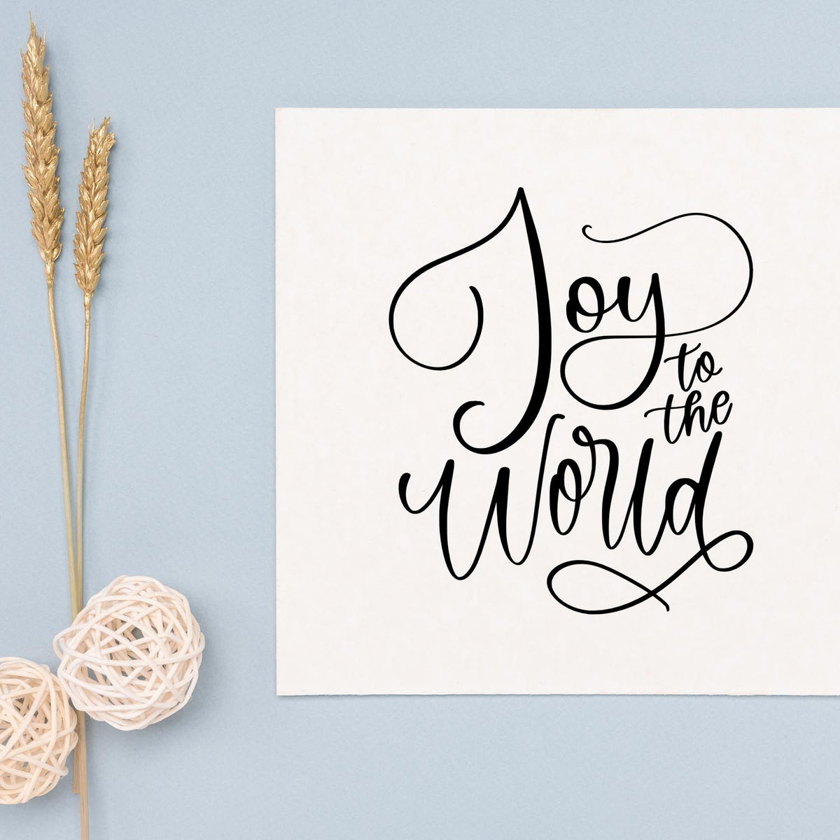 Joy to the World calligraphy rubber stamp design on white card with soft blue background and rustic decor.