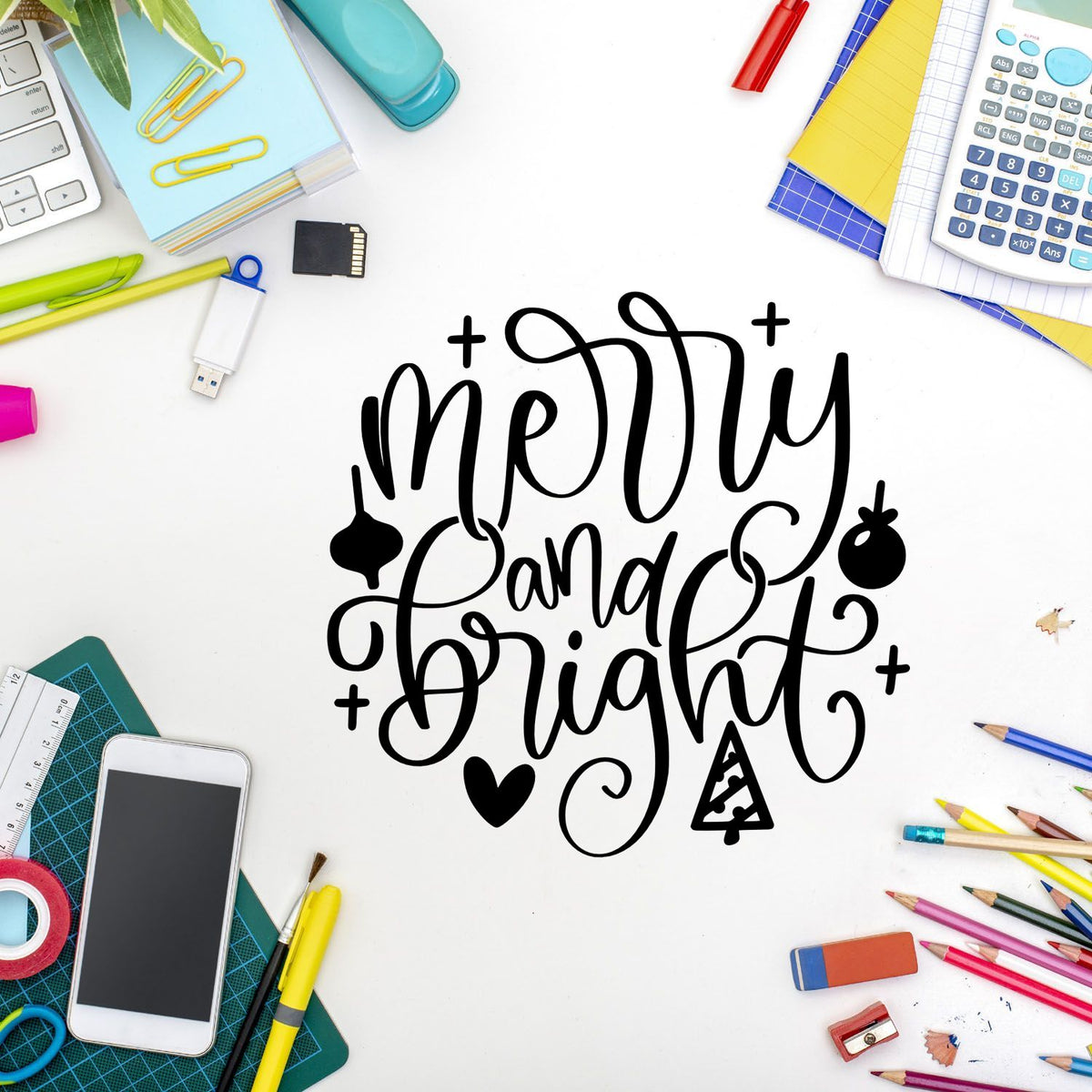 Merry and Bright Christmas rubber stamp design with hand-lettered holiday typography and festive icons on a white desk.
