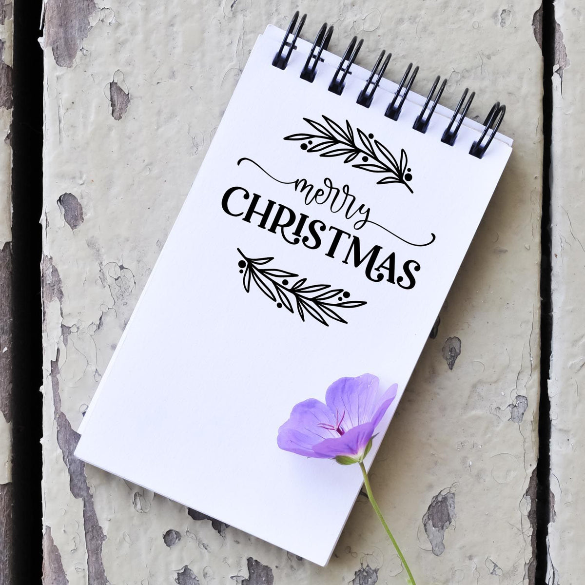 Merry Christmas rubber stamp design with botanical wreath on white spiral notebook, ideal for festive holiday crafting and card making