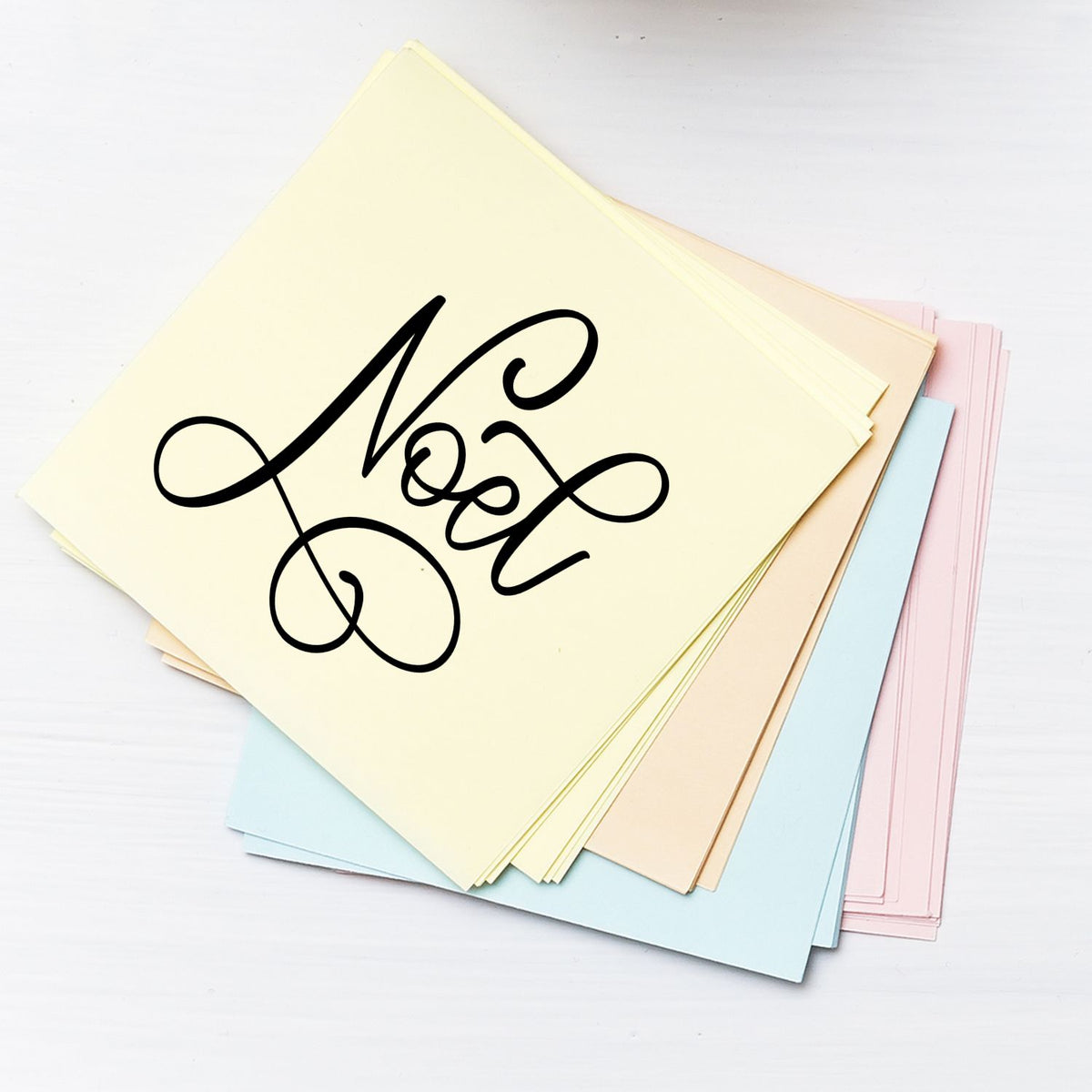 Noel rubber stamp design on pastel paper, ideal for holiday cards, scrapbooking, and custom stationery.