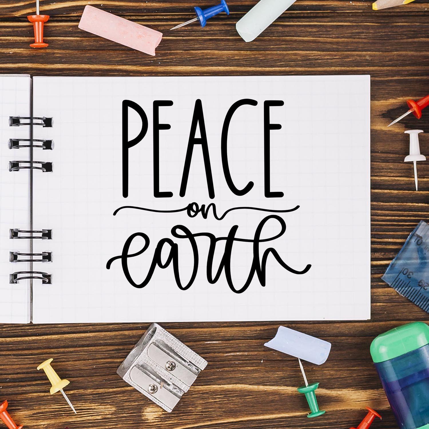 Peace on Earth rubber stamp design on notebook, surrounded by stationery on a rustic wood desk.