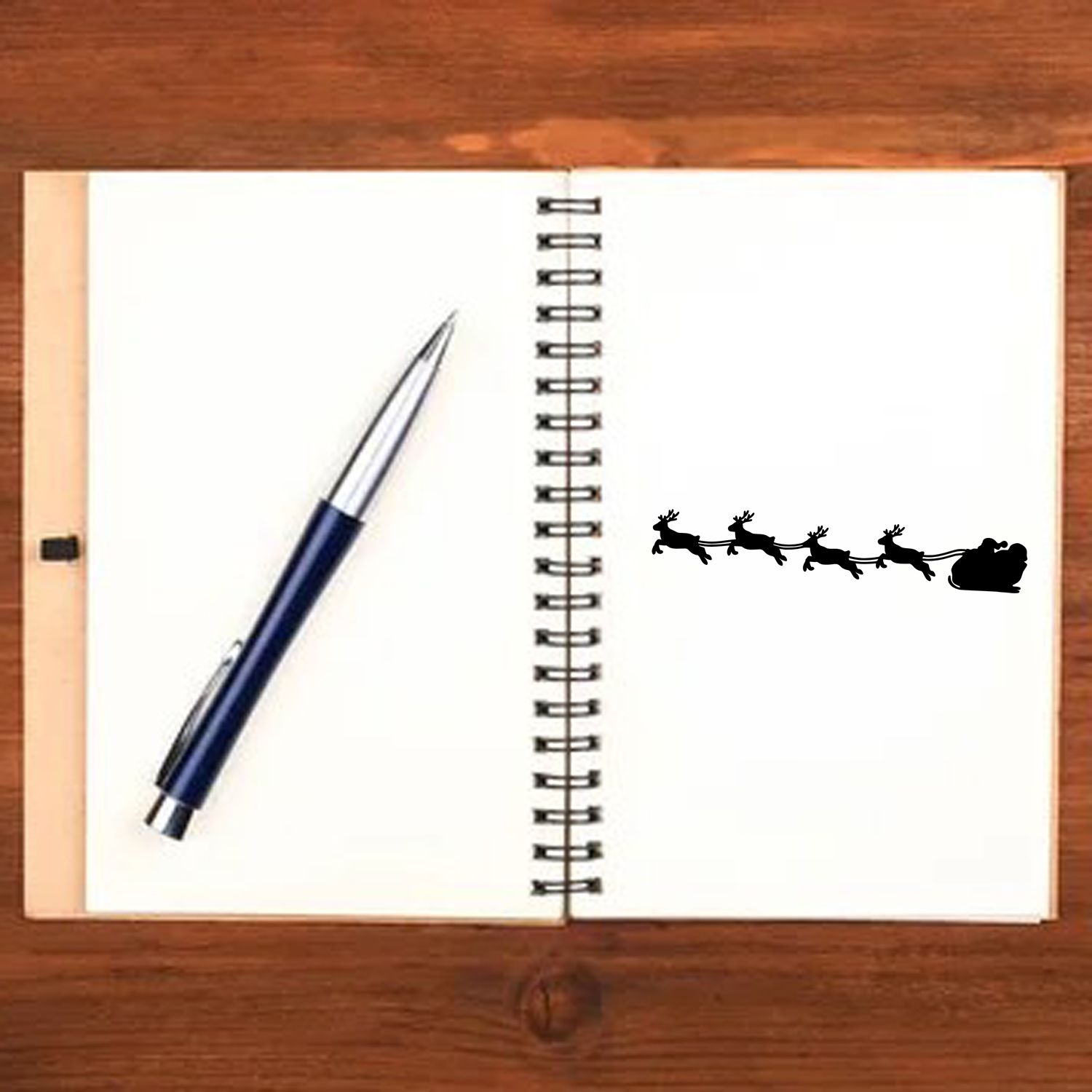 Christmas rubber stamp with Santa sleigh and reindeer on an open notebook, ideal for holiday cards, journaling, and crafts.