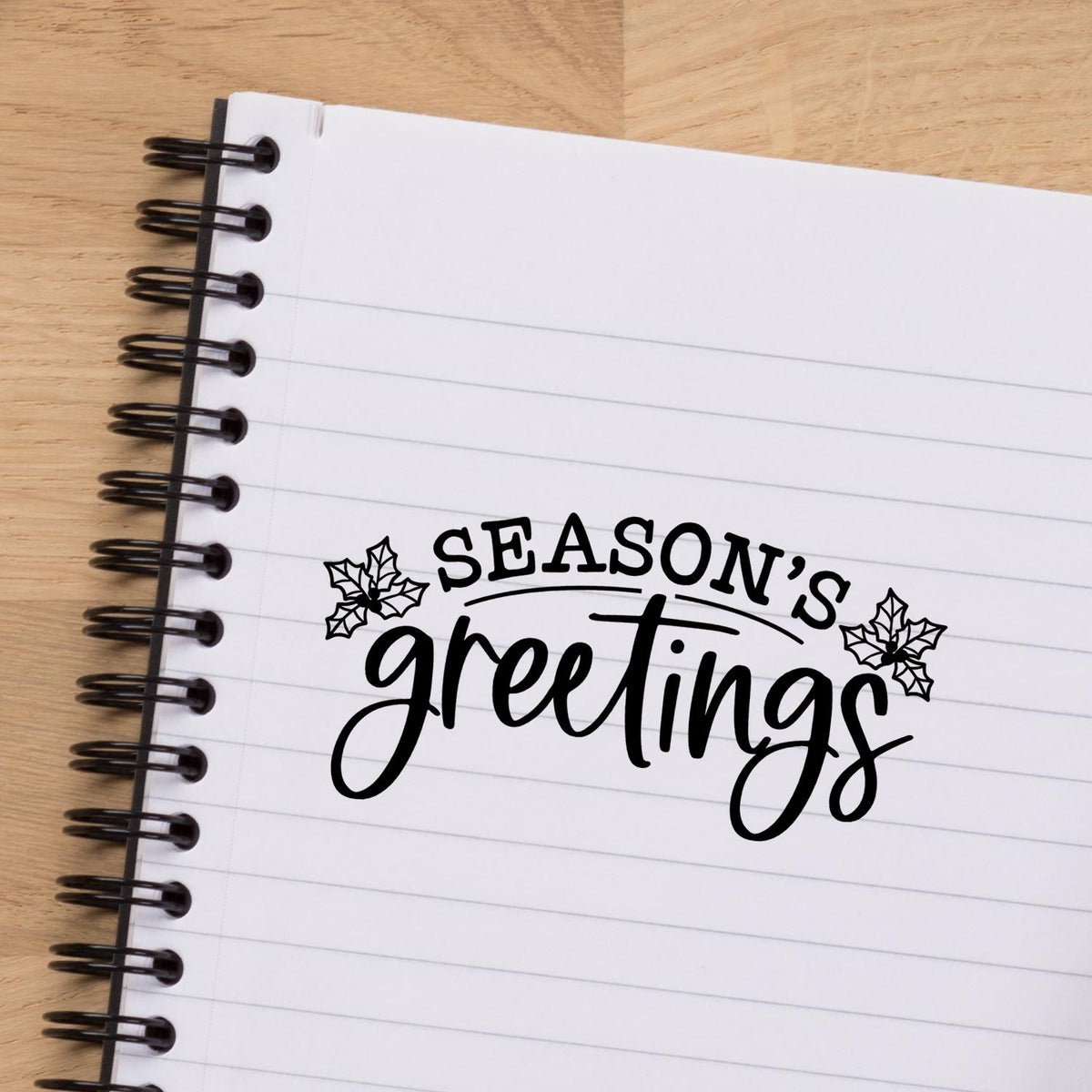 Seasons Greetings holiday rubber stamp with holly design on a notebook page for festive card making.