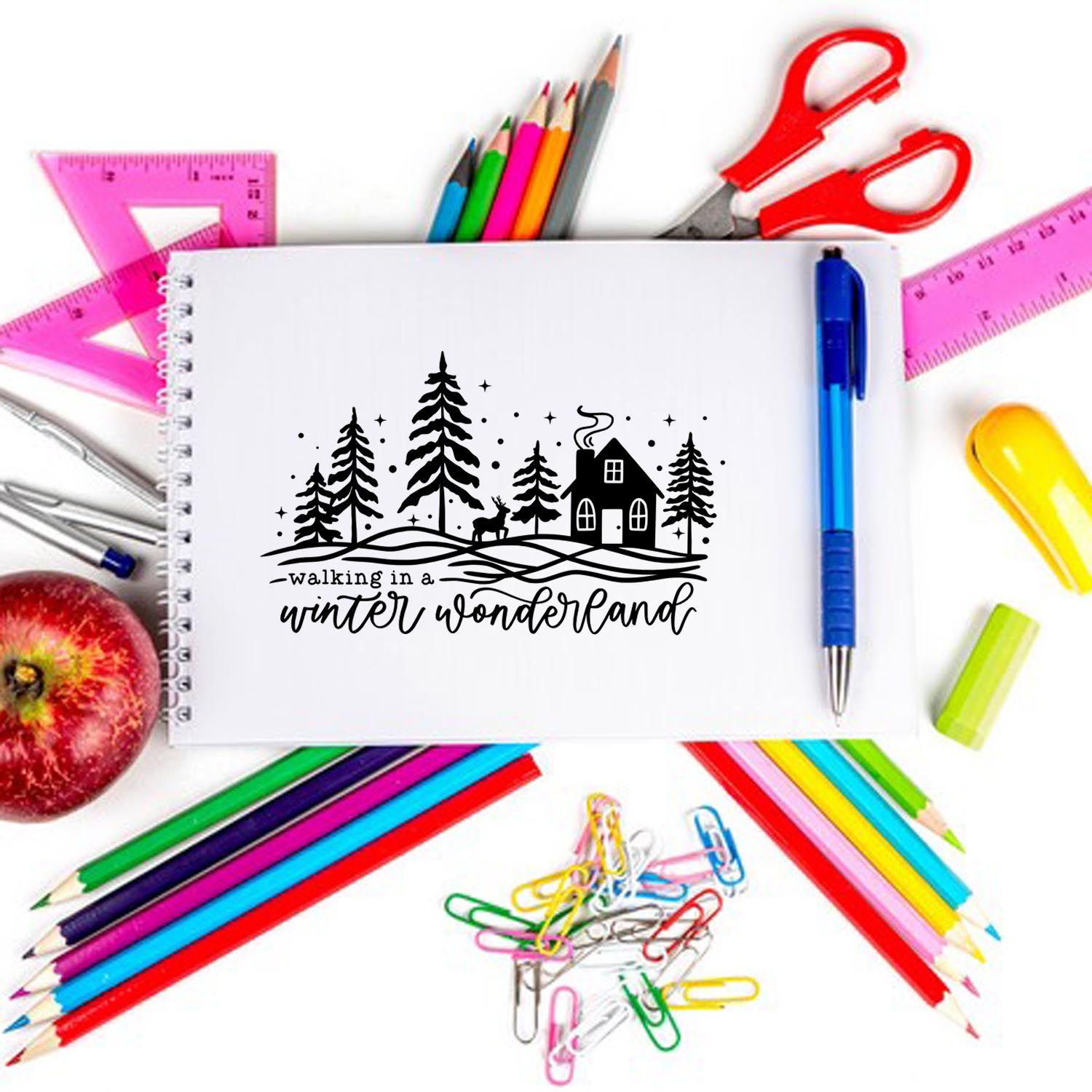 Winter wonderland rubber stamp design on a notebook, surrounded by school supplies and craft tools.