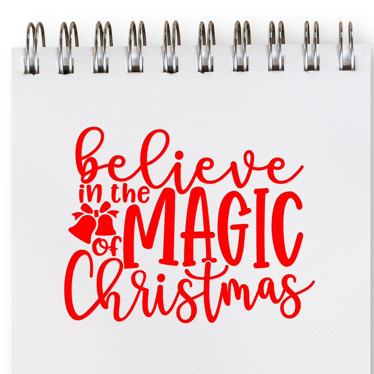 Red Believe in the Magic of Christmas rubber stamp design on spiral notebook page with bells icon for holiday crafts.