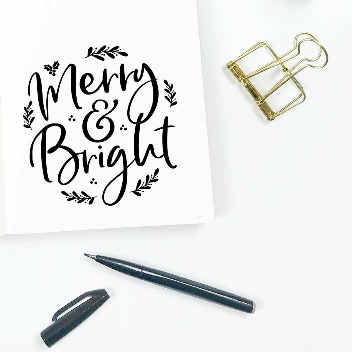 Merry & Bright Christmas rubber stamp design for holiday cards, shown on paper with pen and clip.