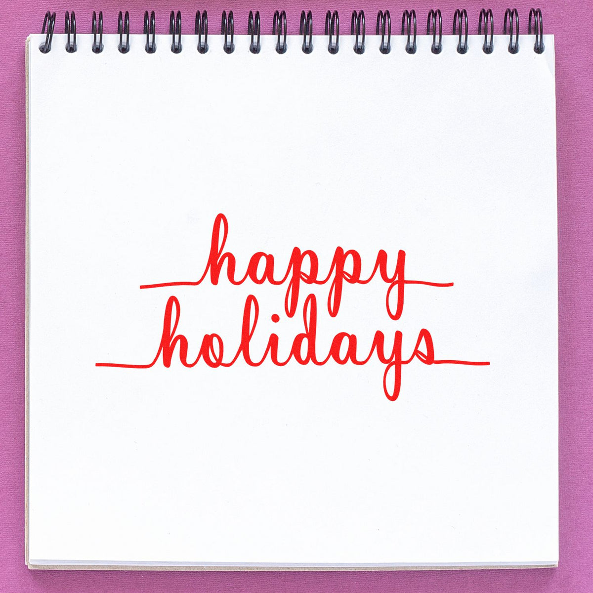 Happy Holidays rubber stamp in red script on a spiral notebook, ideal for holiday cards, crafts and festive packaging.