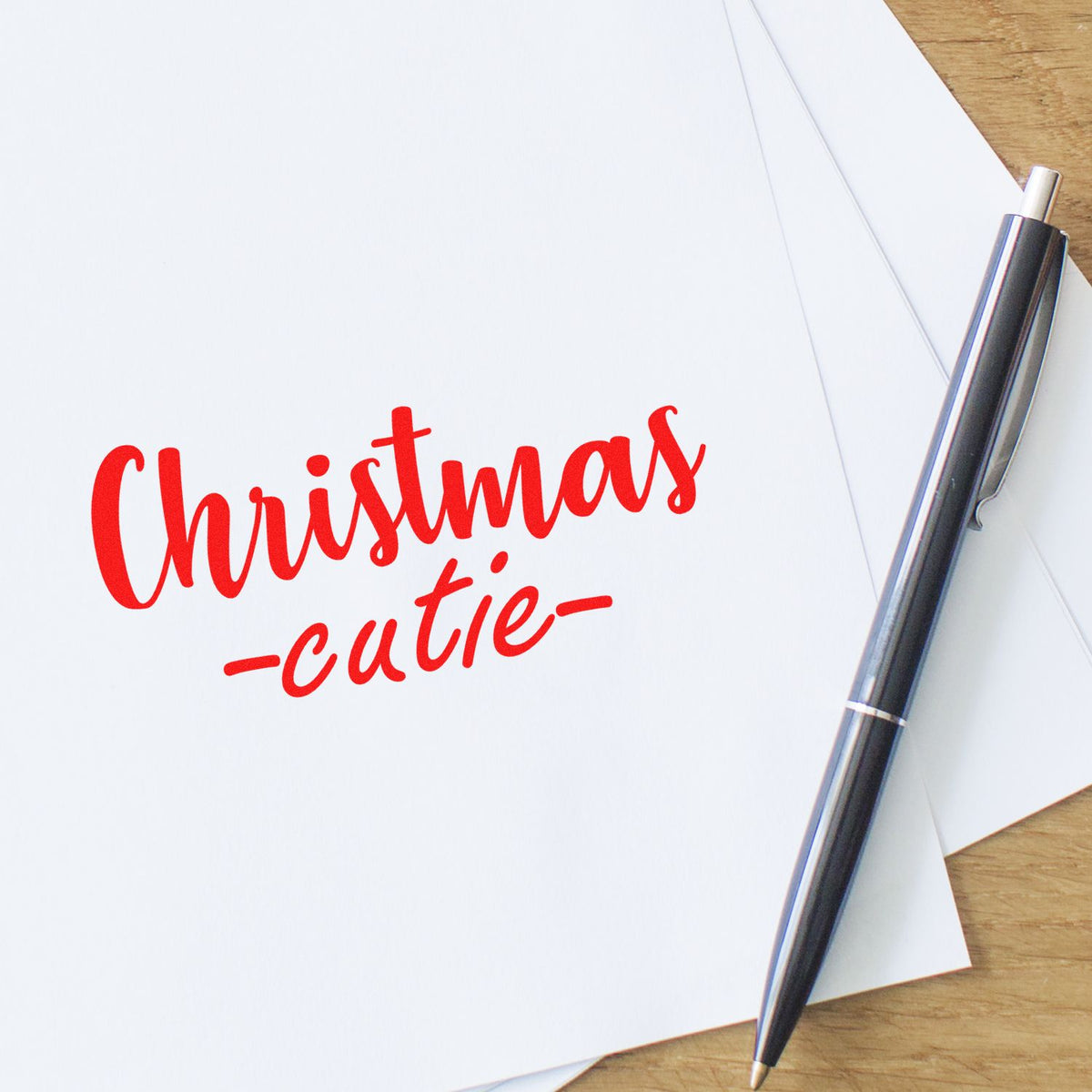Custom Christmas rubber stamp with red Christmas cutie text on paper next to a pen.
