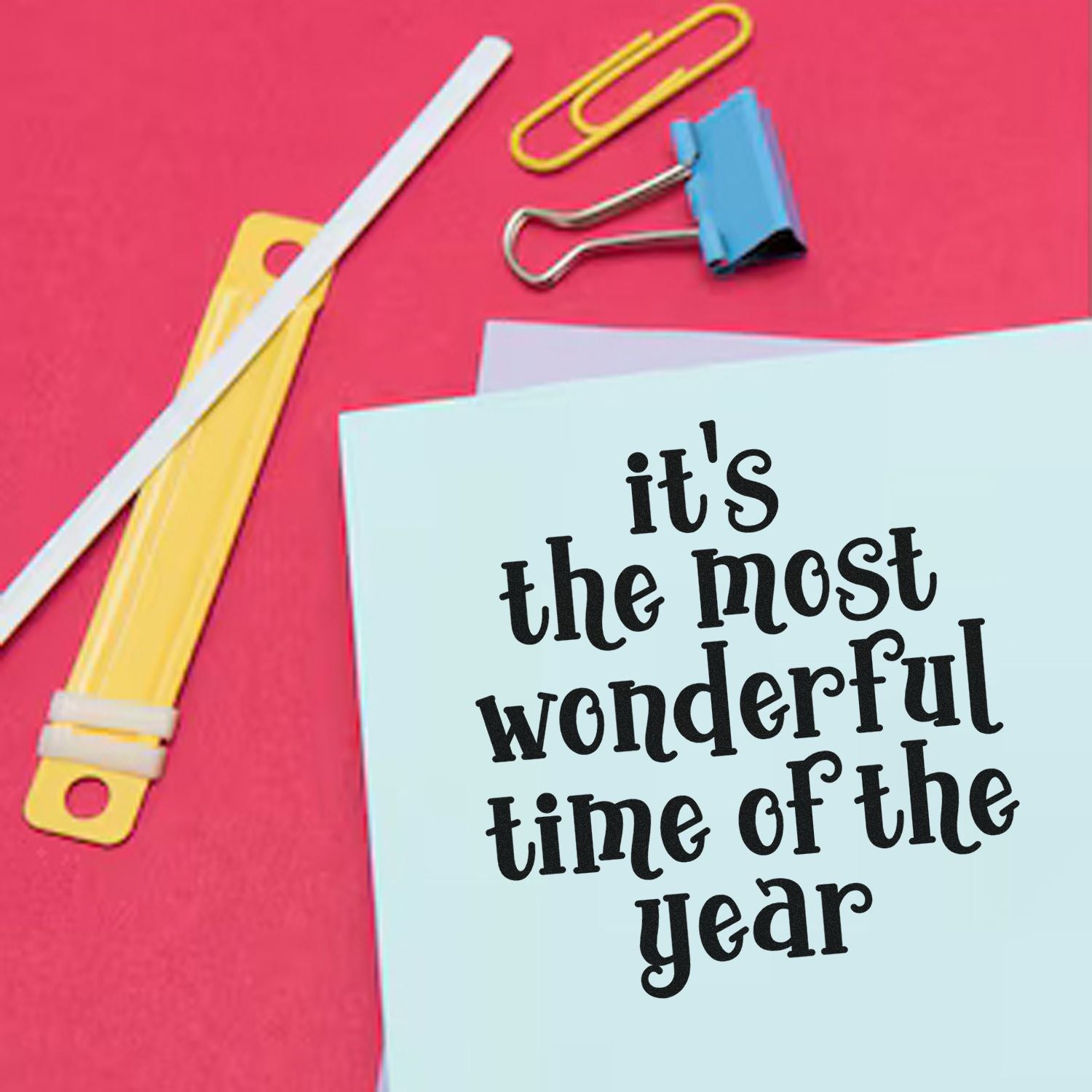 Rubber stamp-style holiday greeting card reading Its the most wonderful time of the year with stationery clips and paper.