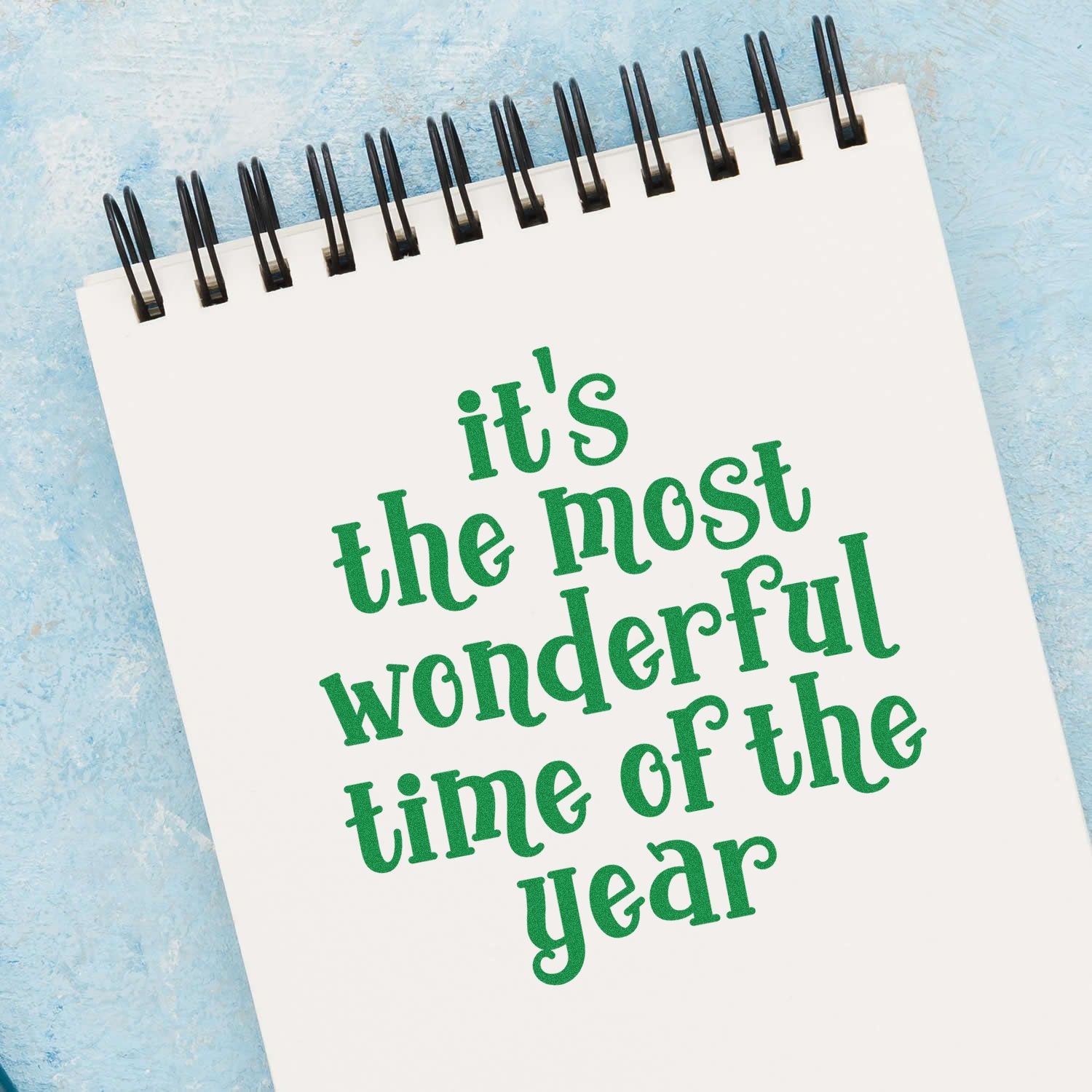 Christmas rubber stamp design on a spiral notebook reading its the most wonderful time of the year in green text.