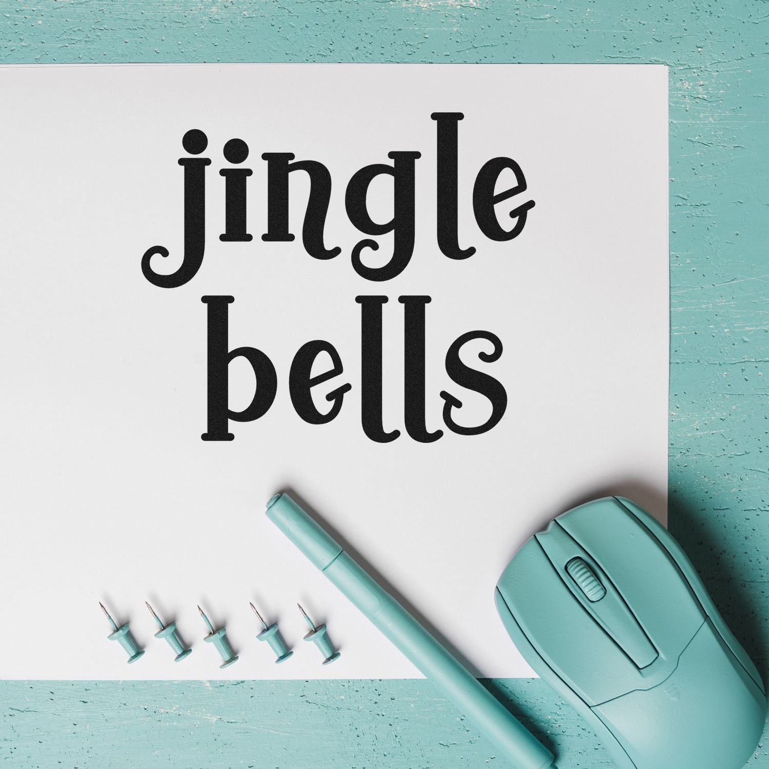 Jingle Bells holiday rubber stamp mockup with vintage black lettering on white paper and mint craft tools.