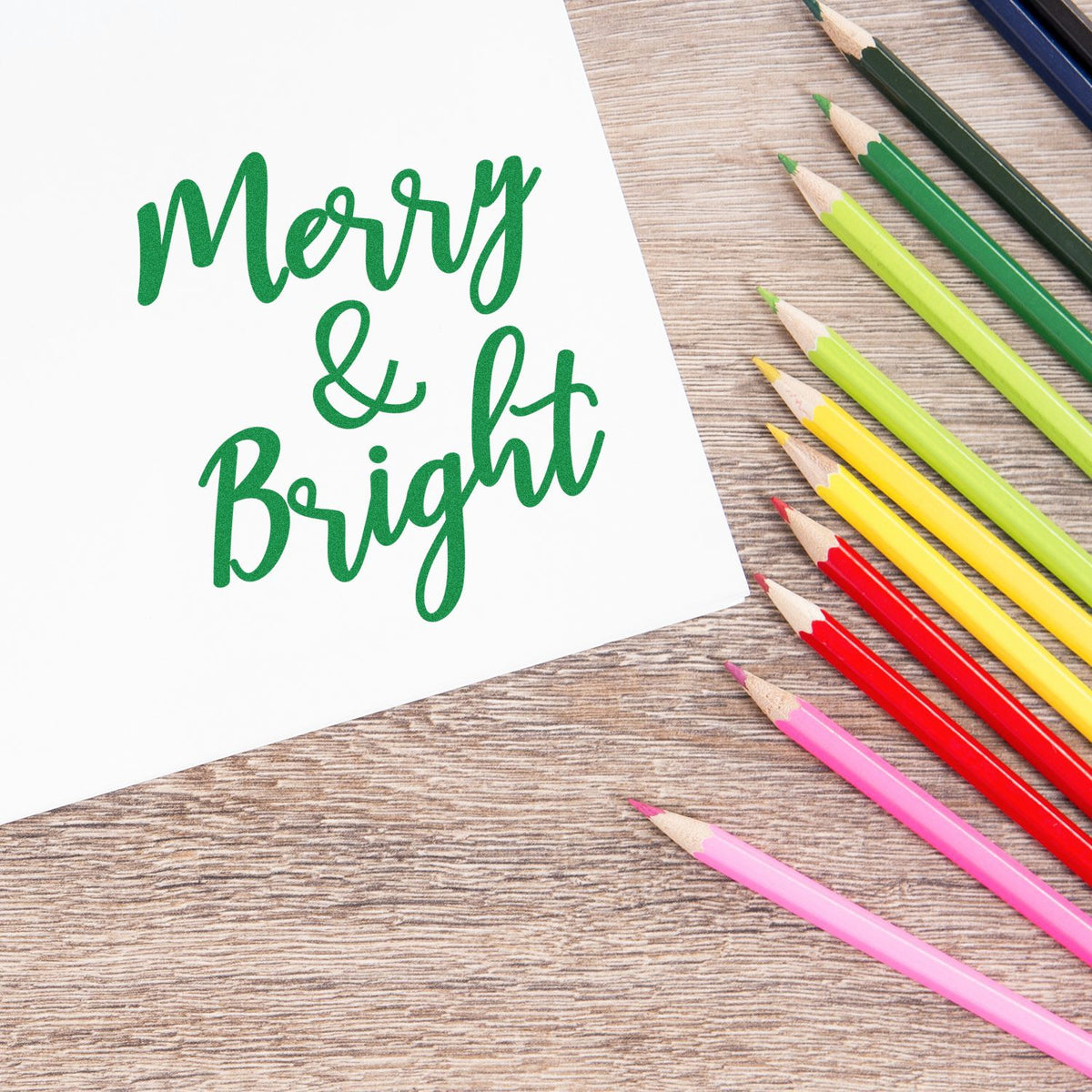 Merry & Bright Christmas rubber stamp design in green script, styled with colorful pencils on a wood background.