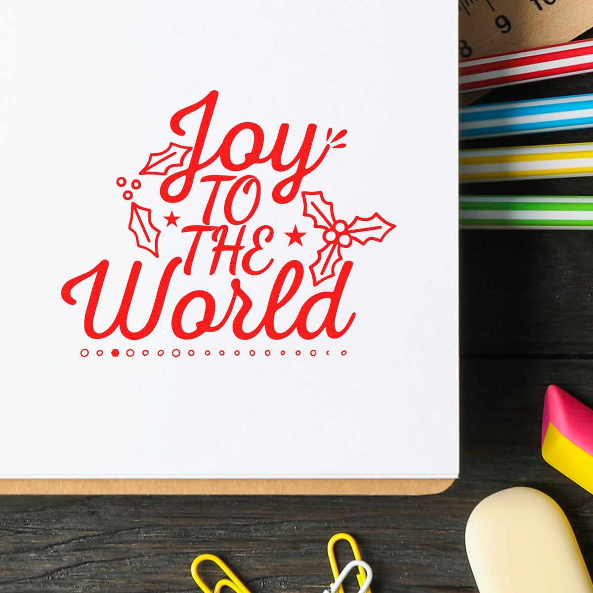 Holiday rubber stamp design with red Joy to the World lettering and festive holly accents on white paper.