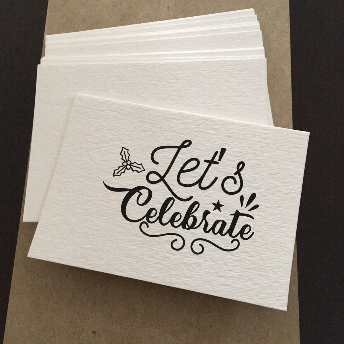 Custom rubber stamp design on white napkins reading Lets Celebrate with holly detail, ideal for holiday party favors and events.