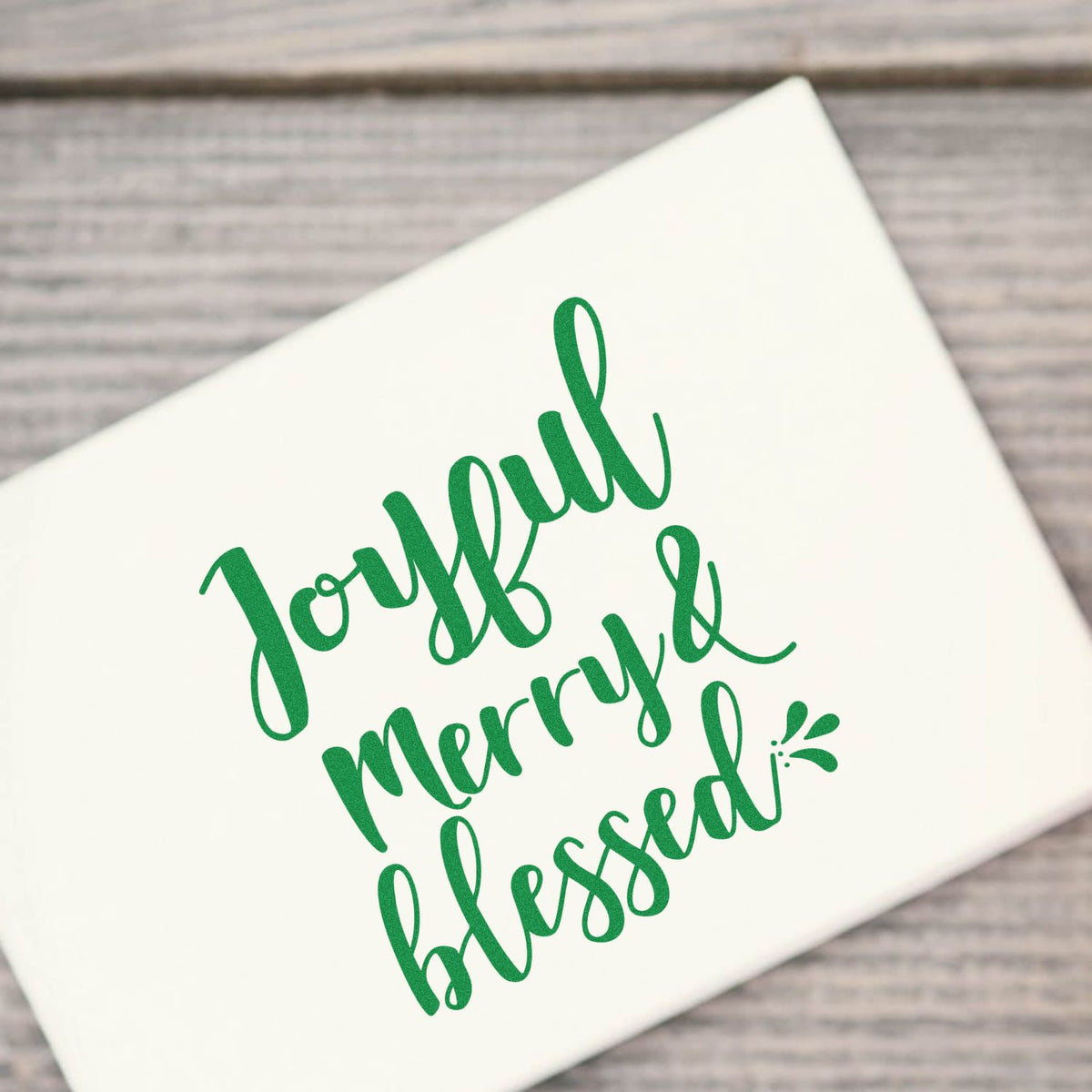 Green Joyful Merry & Blessed holiday rubber stamp design on white gift box, ideal for festive Christmas packaging.