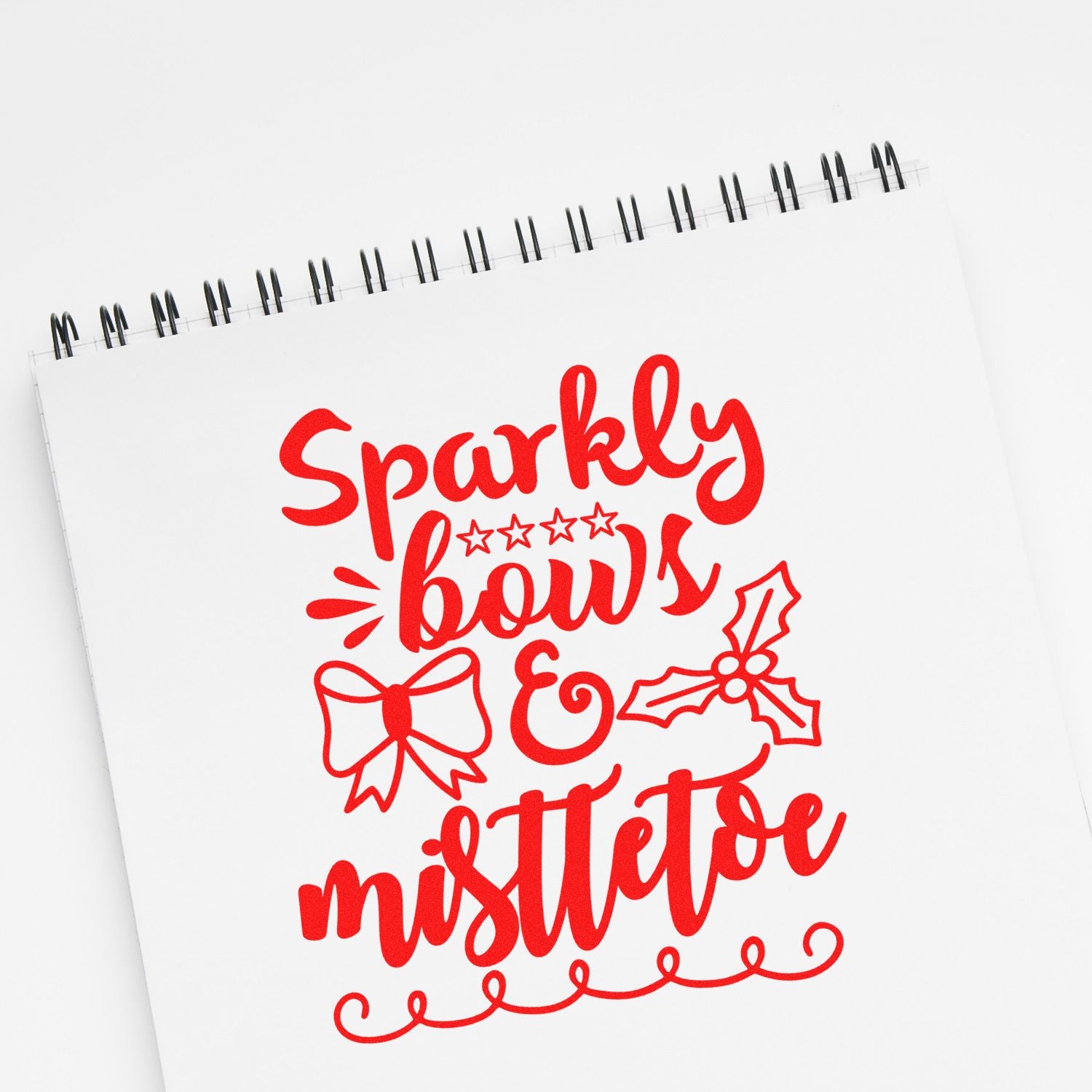 Christmas rubber stamp design with sparkly bows and mistletoe in red script on a notebook page.
