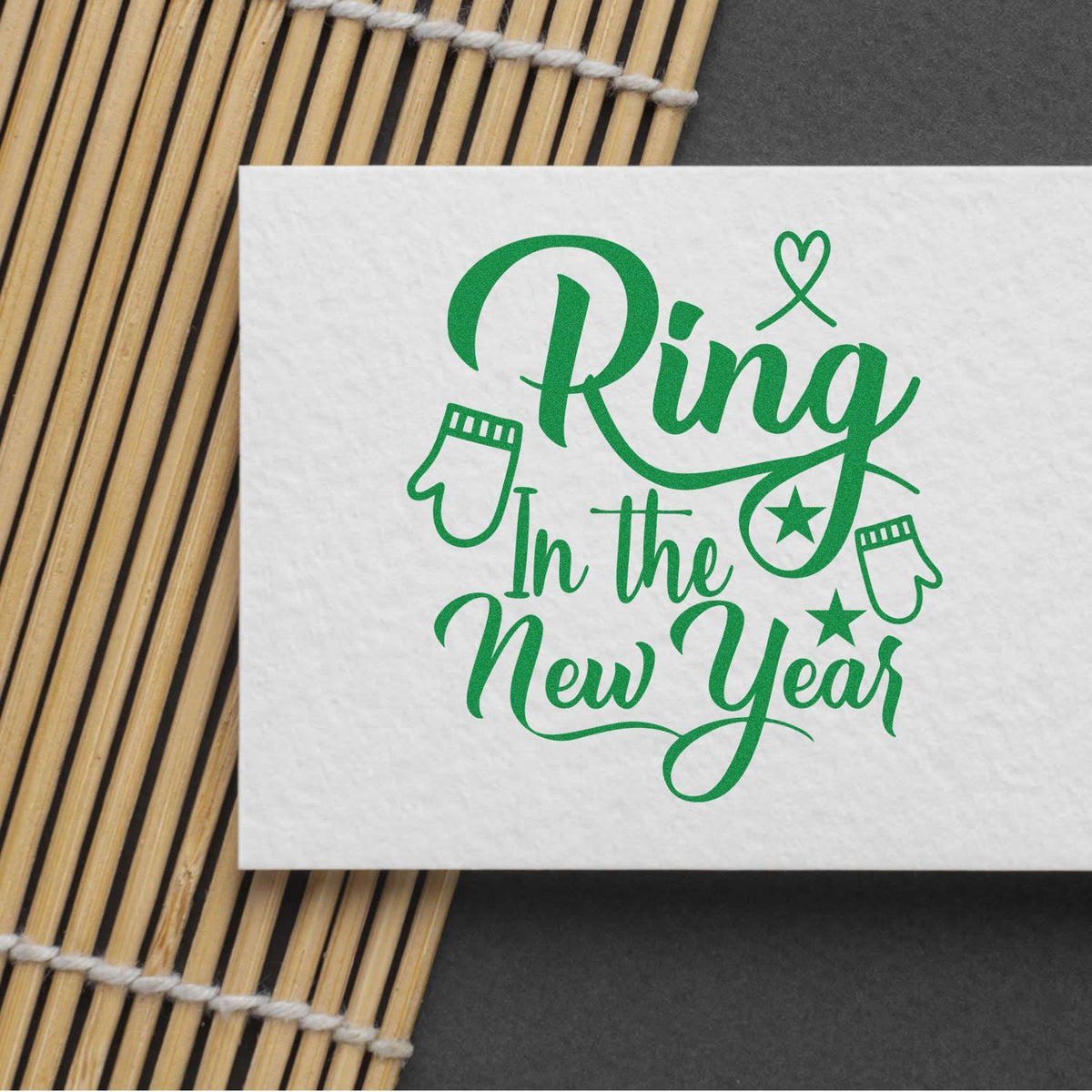 Green "Ring in the New Year" rubber stamp design with mittens and stars, stamped on white paper.