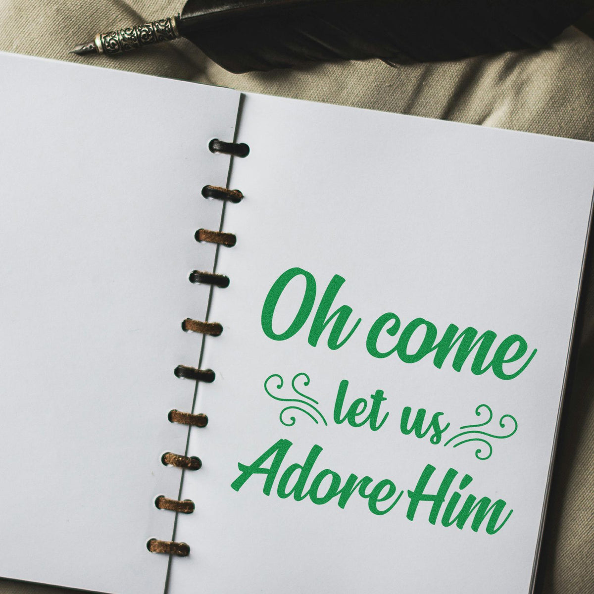 Christmas scripture rubber stamp design reading Oh come let us adore Him on a notebook page.