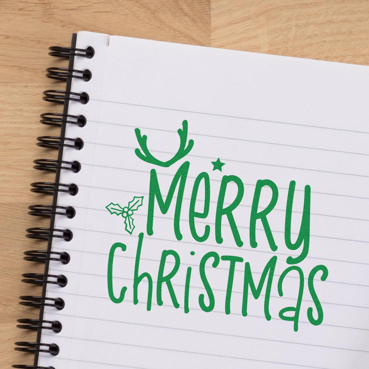 Merry Christmas rubber stamp design stamped in green on a lined notebook, featuring festive antlers and holly.