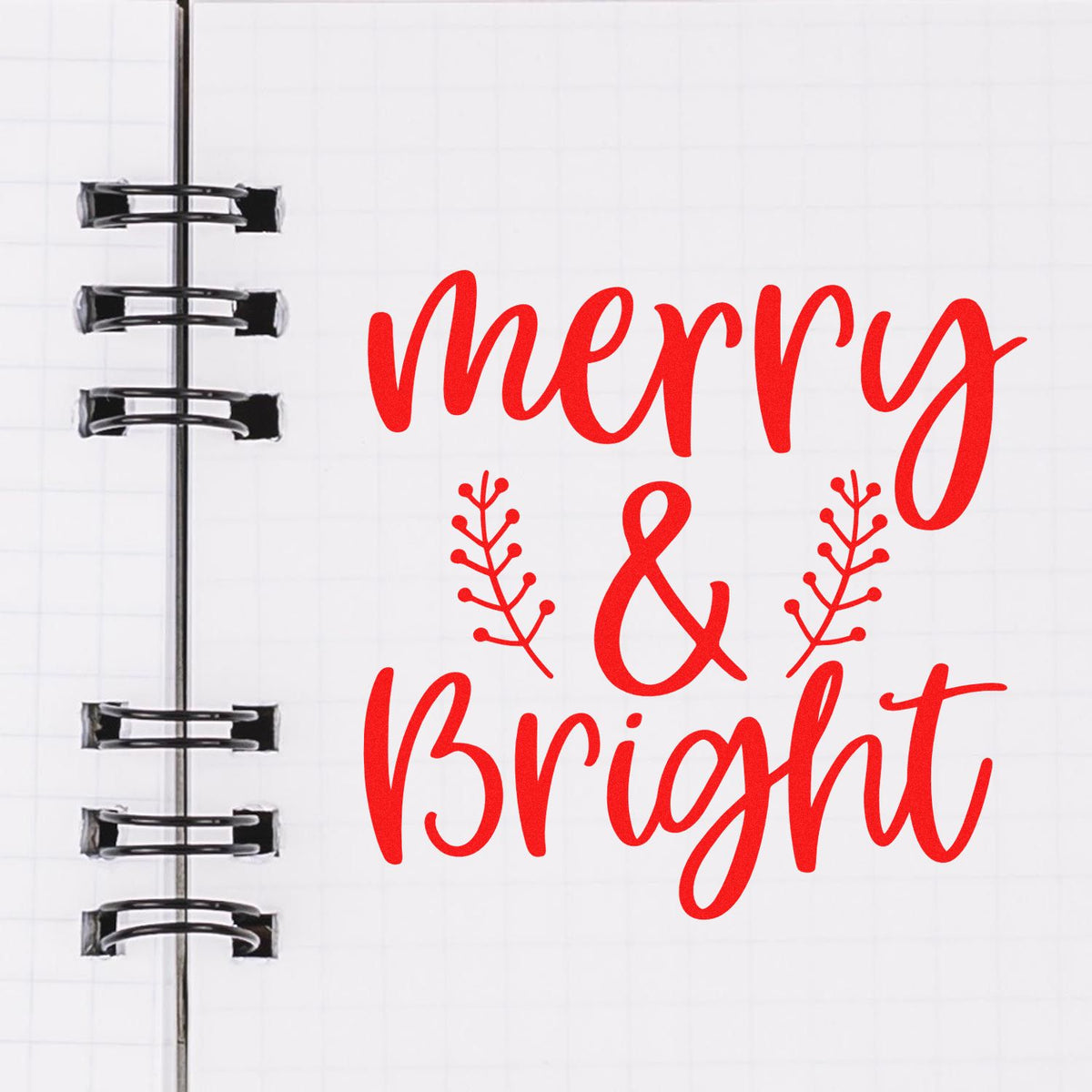 Merry & Bright red calligraphy rubber stamp design with festive branch accents on a notebook page.