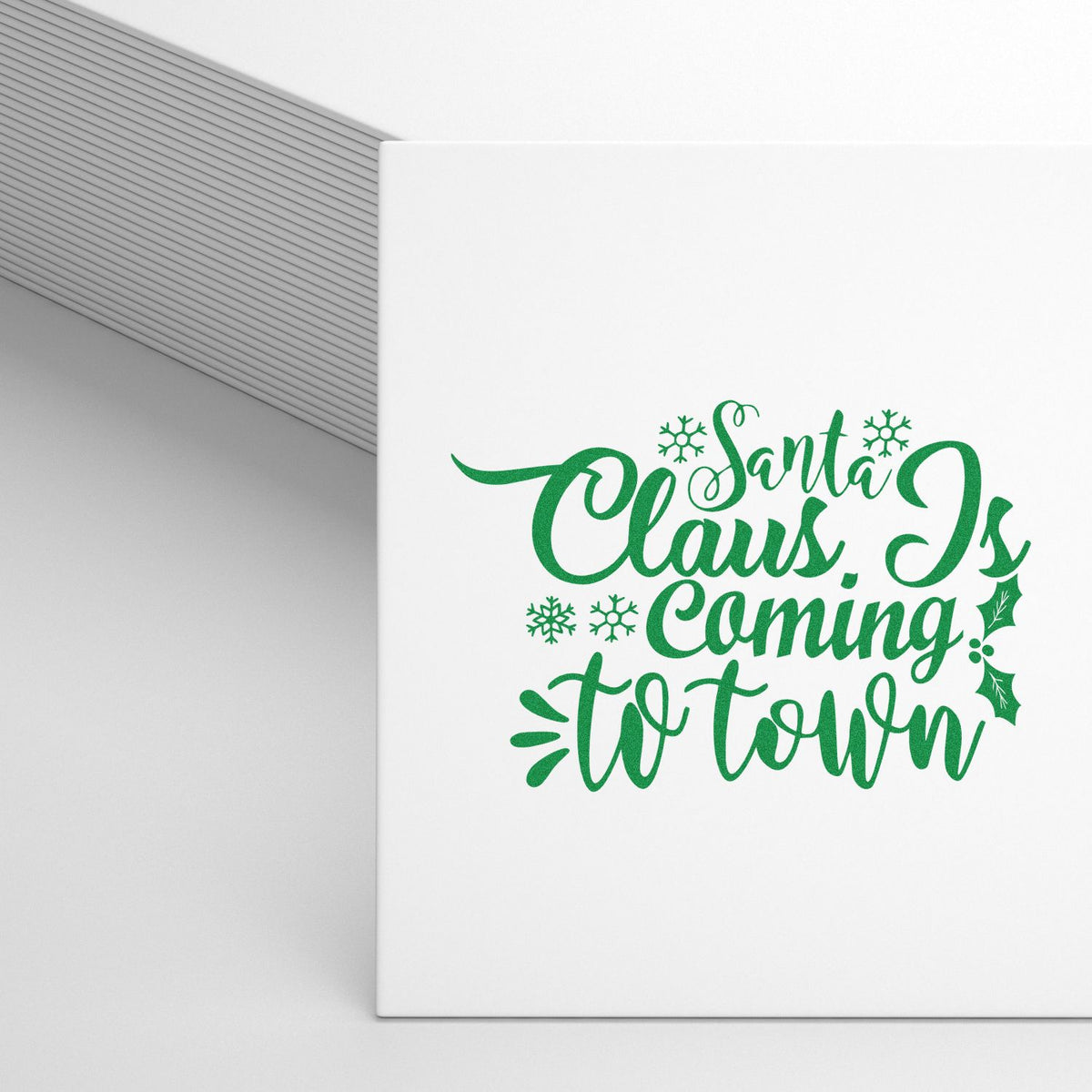 Christmas rubber stamp design reading Santa Claus Is Coming to Town in green with snowflakes and holly accents.