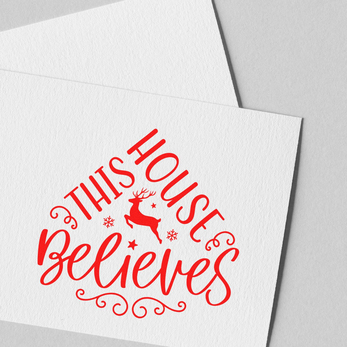 Holiday rubber stamp design reading This House Believes with reindeer and snowflakes on white cardstock.
