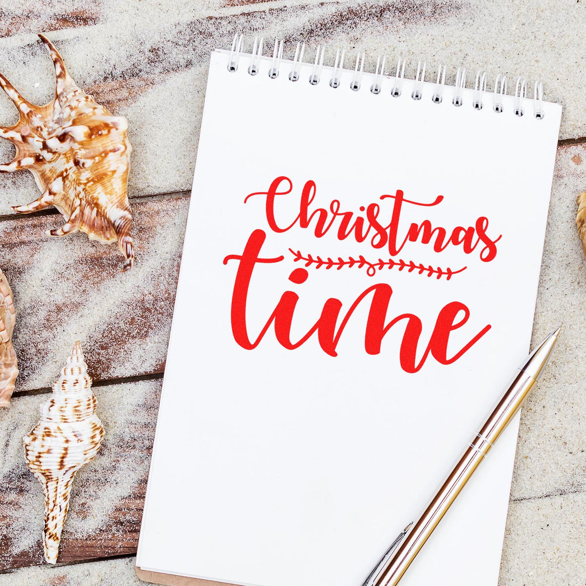 Christmas Time rubber stamp in red script on notebook mockup, styled with seashells and pen for holiday crafting.