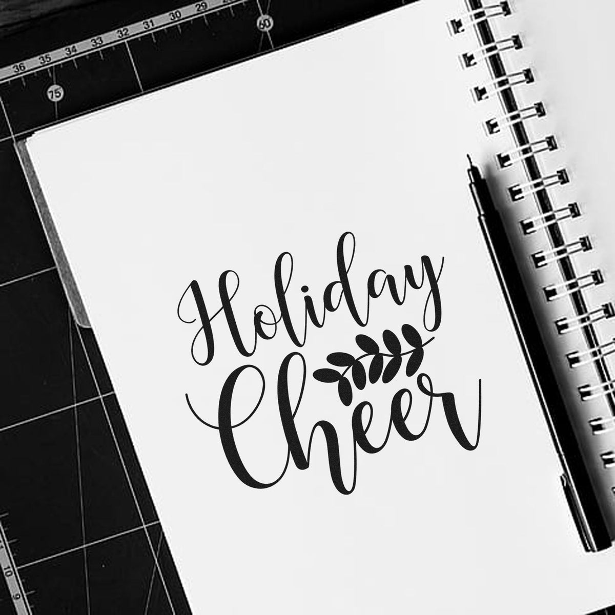 Holiday Cheer script rubber stamp design on notebook page with pen for holiday crafting