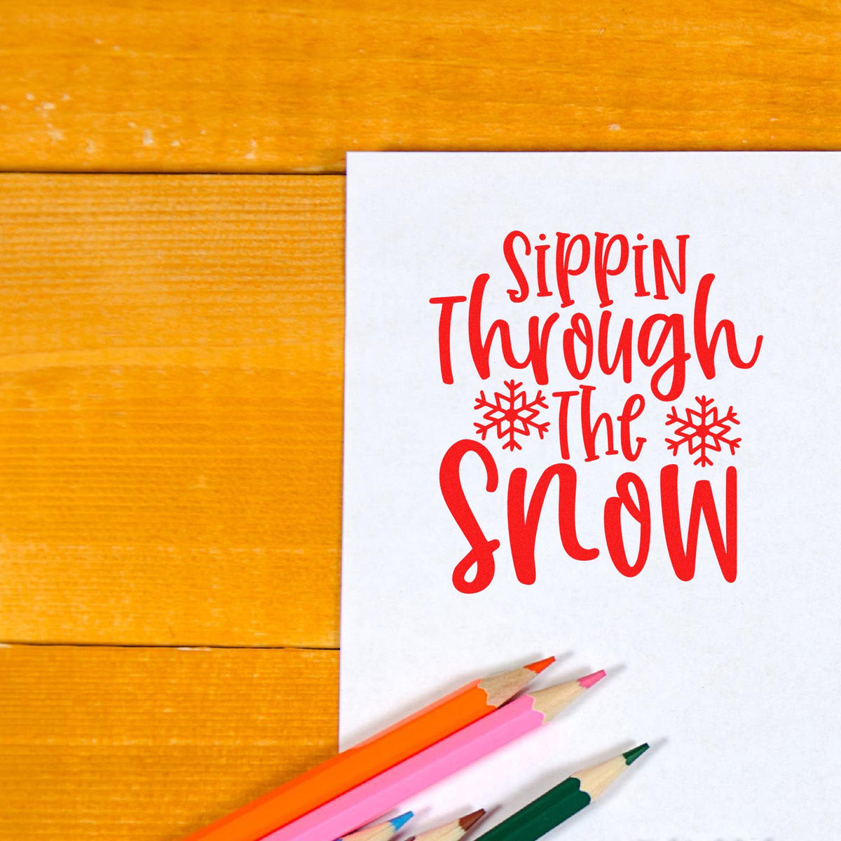 Holiday rubber stamp design reading Sippin Through the Snow in red on white paper with snowflakes and colored pencils.