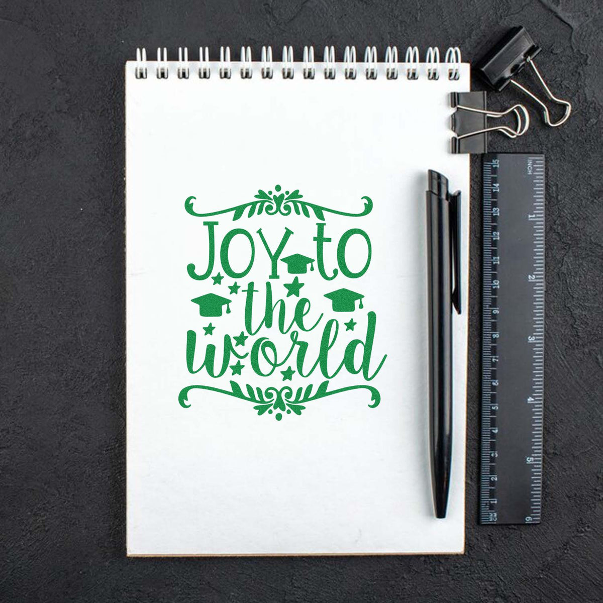 Green Joy to the World graduation rubber stamp design on notebook, perfect for teacher and student crafts.