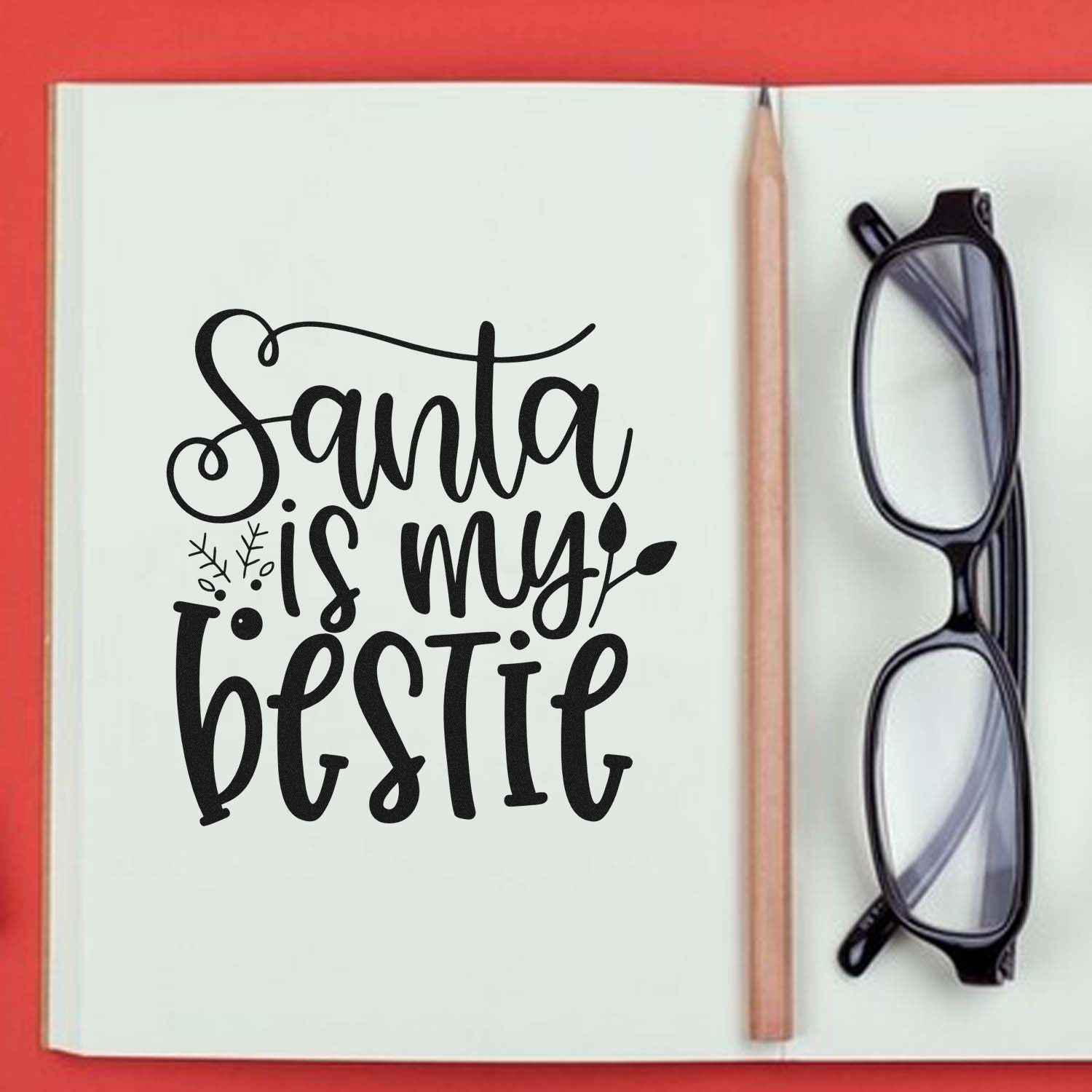 Santa is my Bestie rubber stamp design in playful script, shown in a notebook with pencil and glasses.