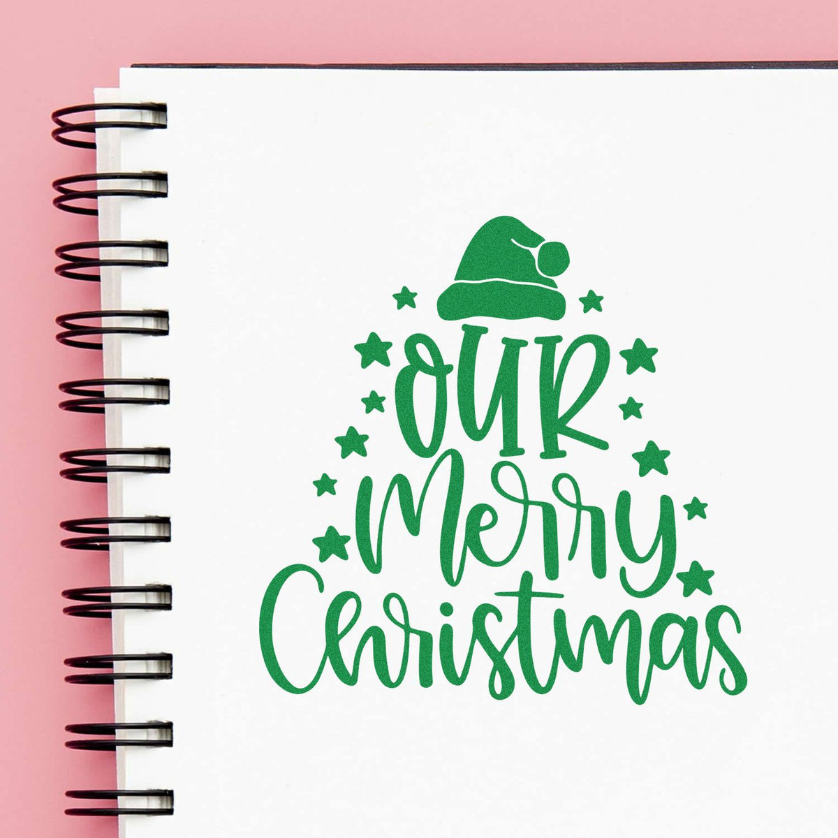 Custom Christmas rubber stamp design reading Our Merry Christmas with Santa hat and stars on a notebook page.
