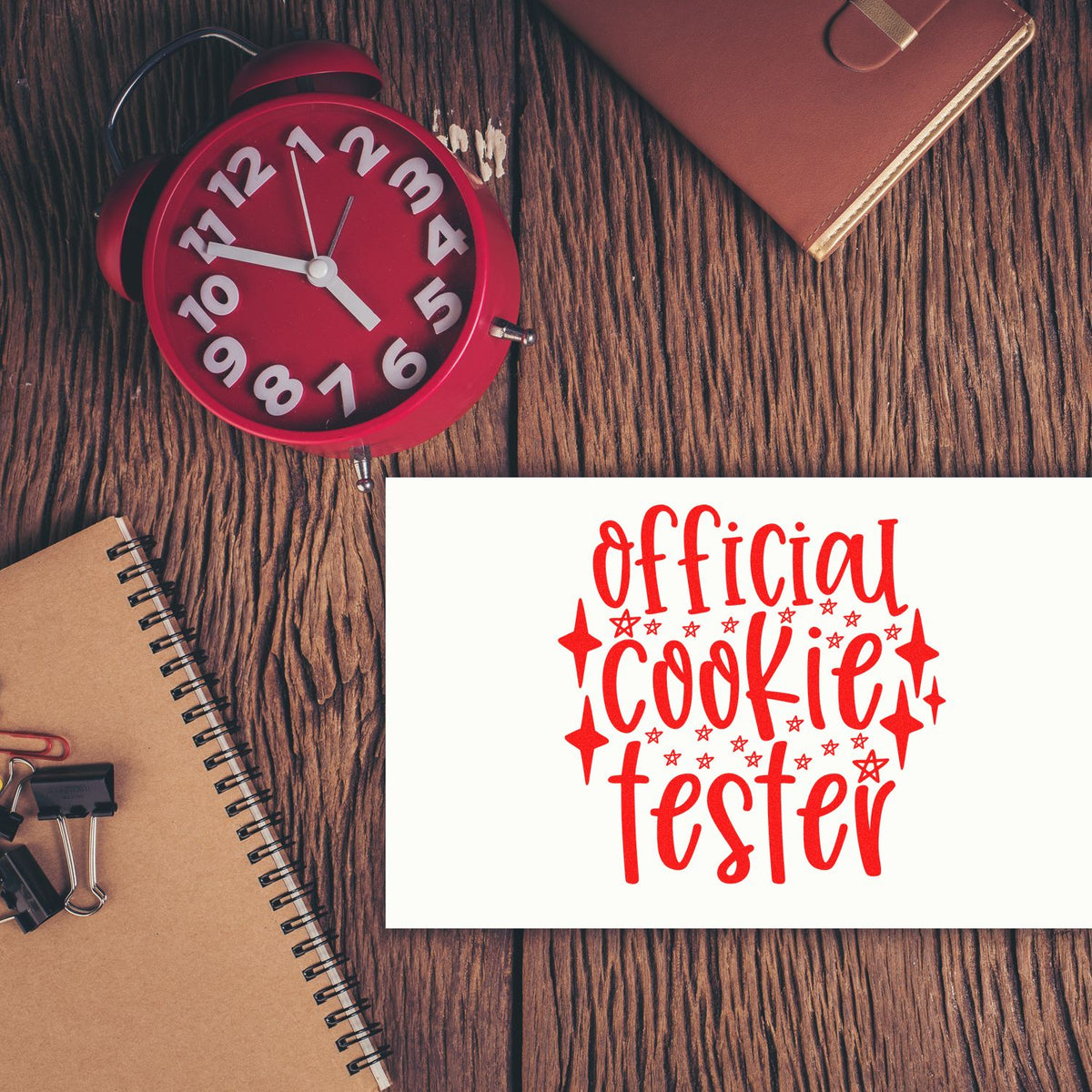 Official cookie tester rubber stamp design mockup with red lettering, displayed on a wooden desk with clock and notebooks.