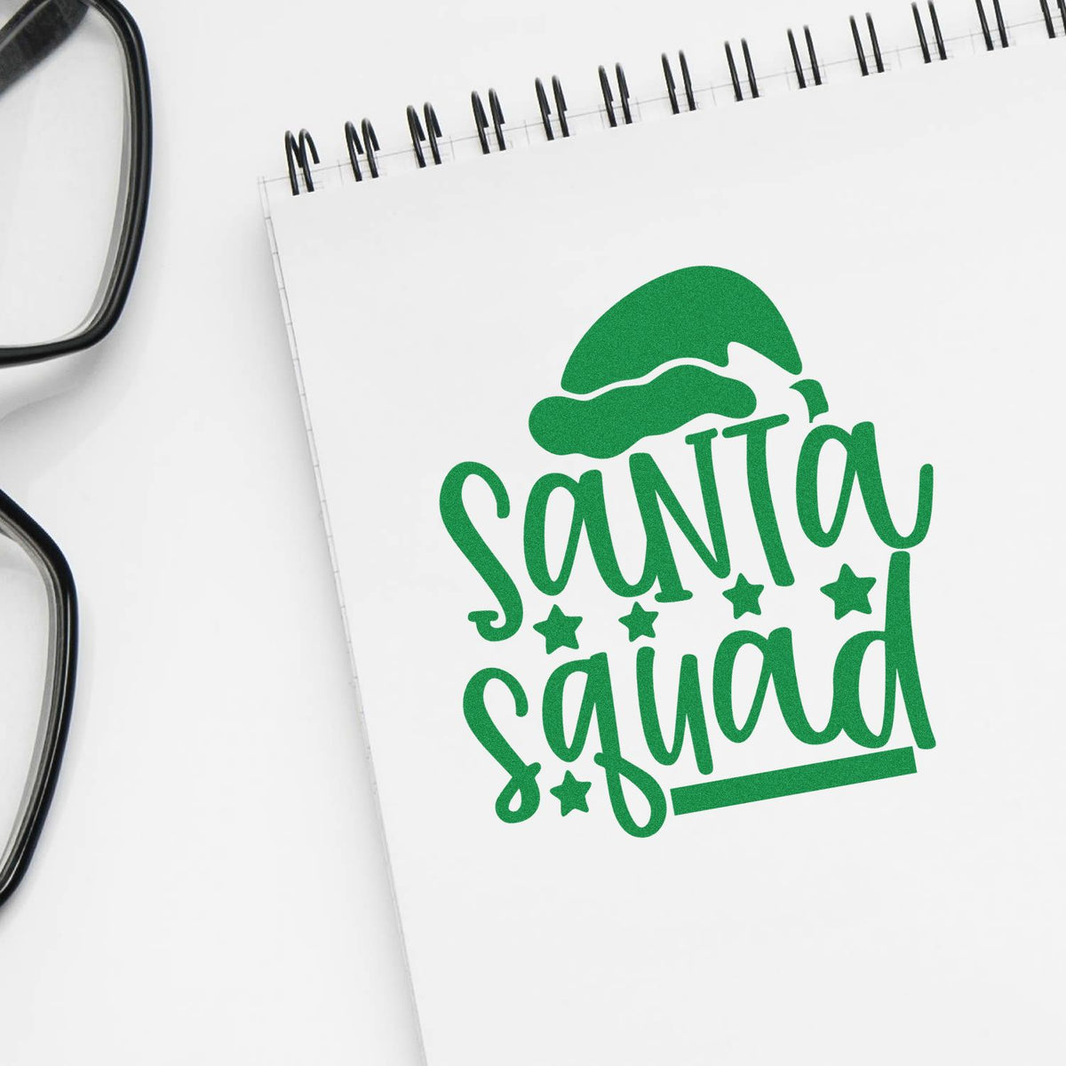 Santa Squad Christmas rubber stamp design on notebook mockup with green Santa hat lettering and stars.