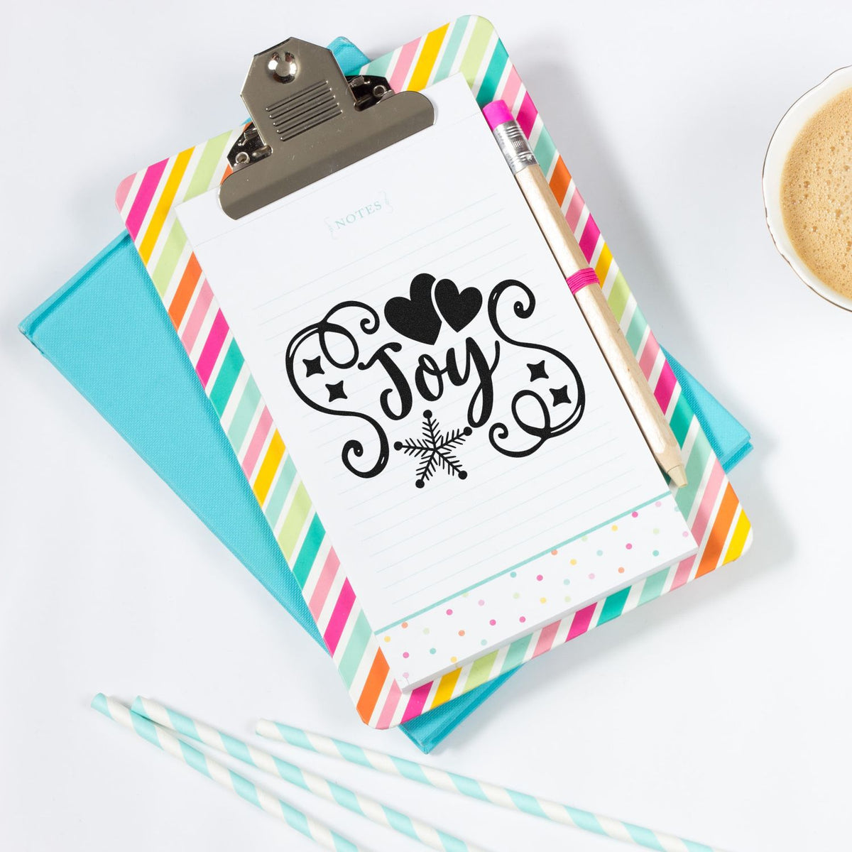 Joy holiday rubber stamp design on notepad clipboard with hearts and snowflake, styled with colorful stationery.