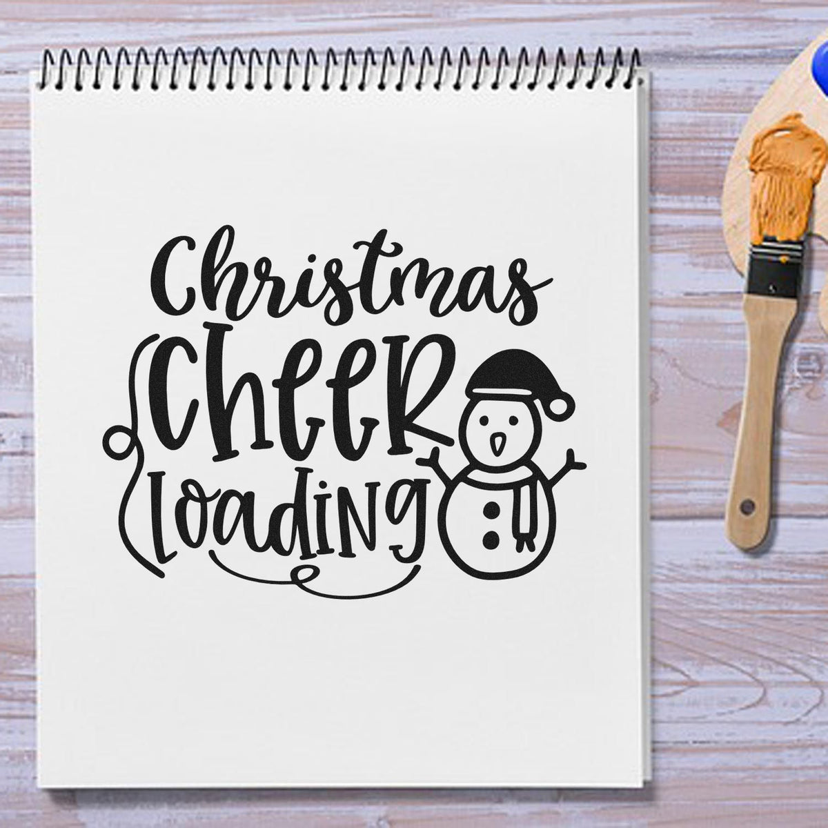 Christmas Cheer Loading Snowman Premium Wooden Stamp - Vintage Pro imprint stamped in black ink. The words "Christmas cheer loading" appear beside a snowman wearing a Santa hat.