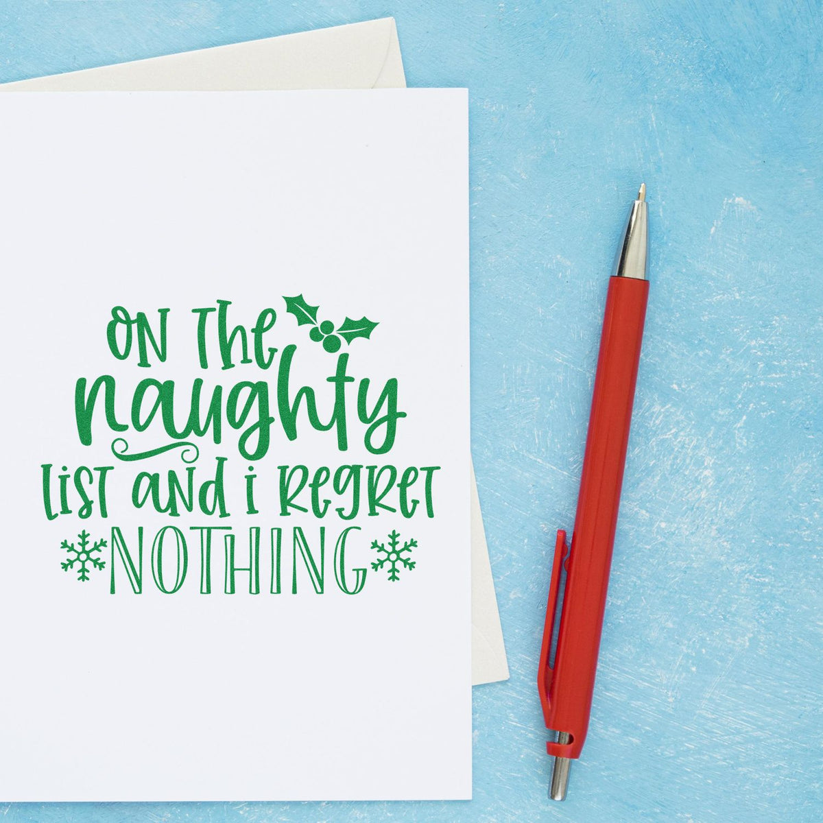 Christmas rubber stamp design on holiday card reading On the naughty list and I regret nothing with holly and snowflakes.