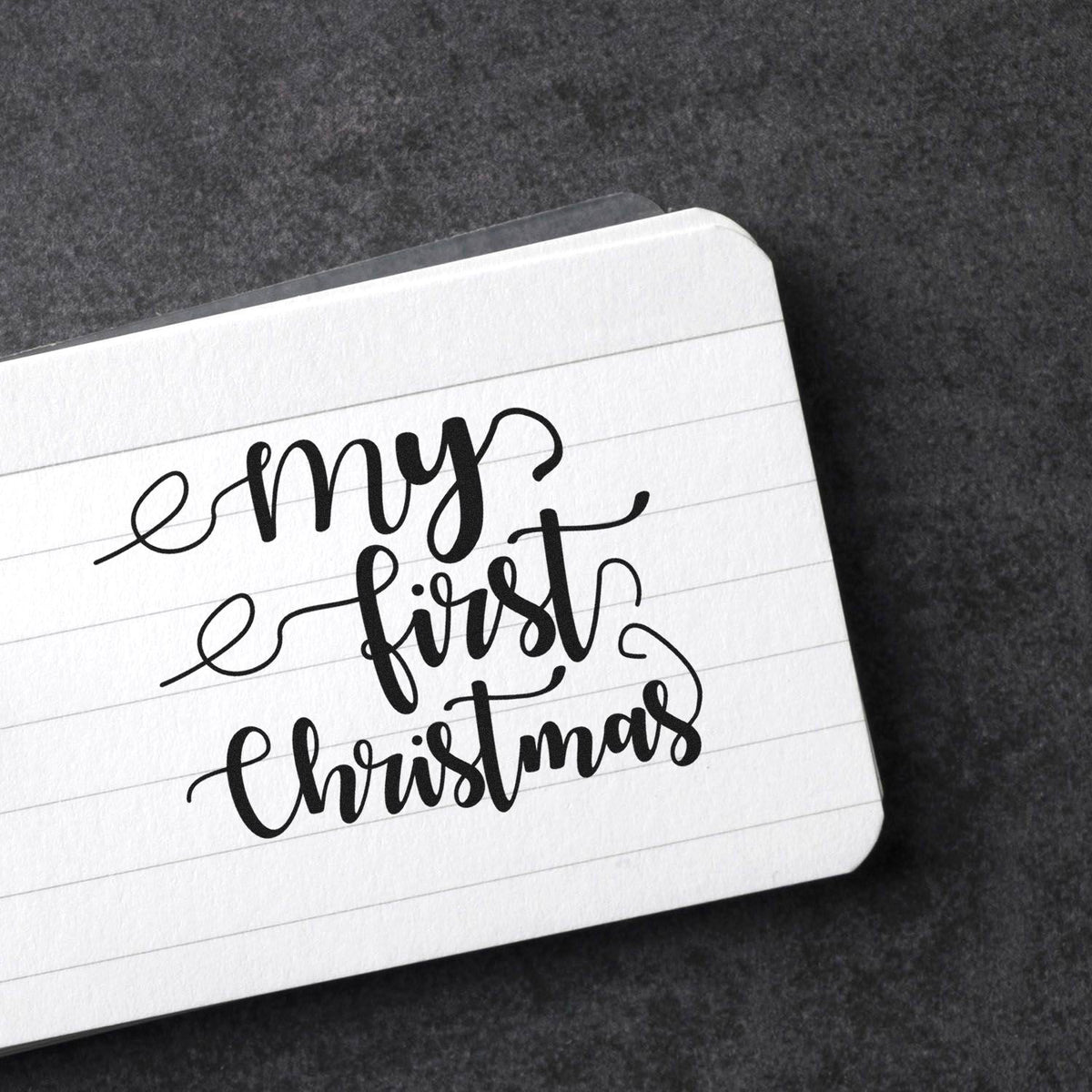 My First Christmas calligraphy rubber stamp mockup on lined paper for holiday cards, scrapbooking, and festive crafts.