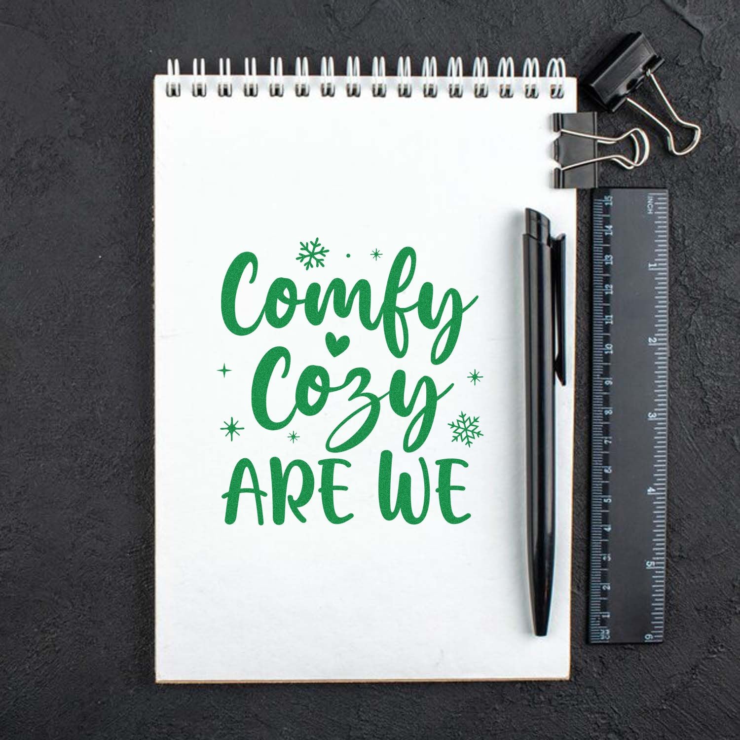 Green Comfy Cozy Are We Christmas rubber stamp design on notebook with snowflakes, pen, and ruler.