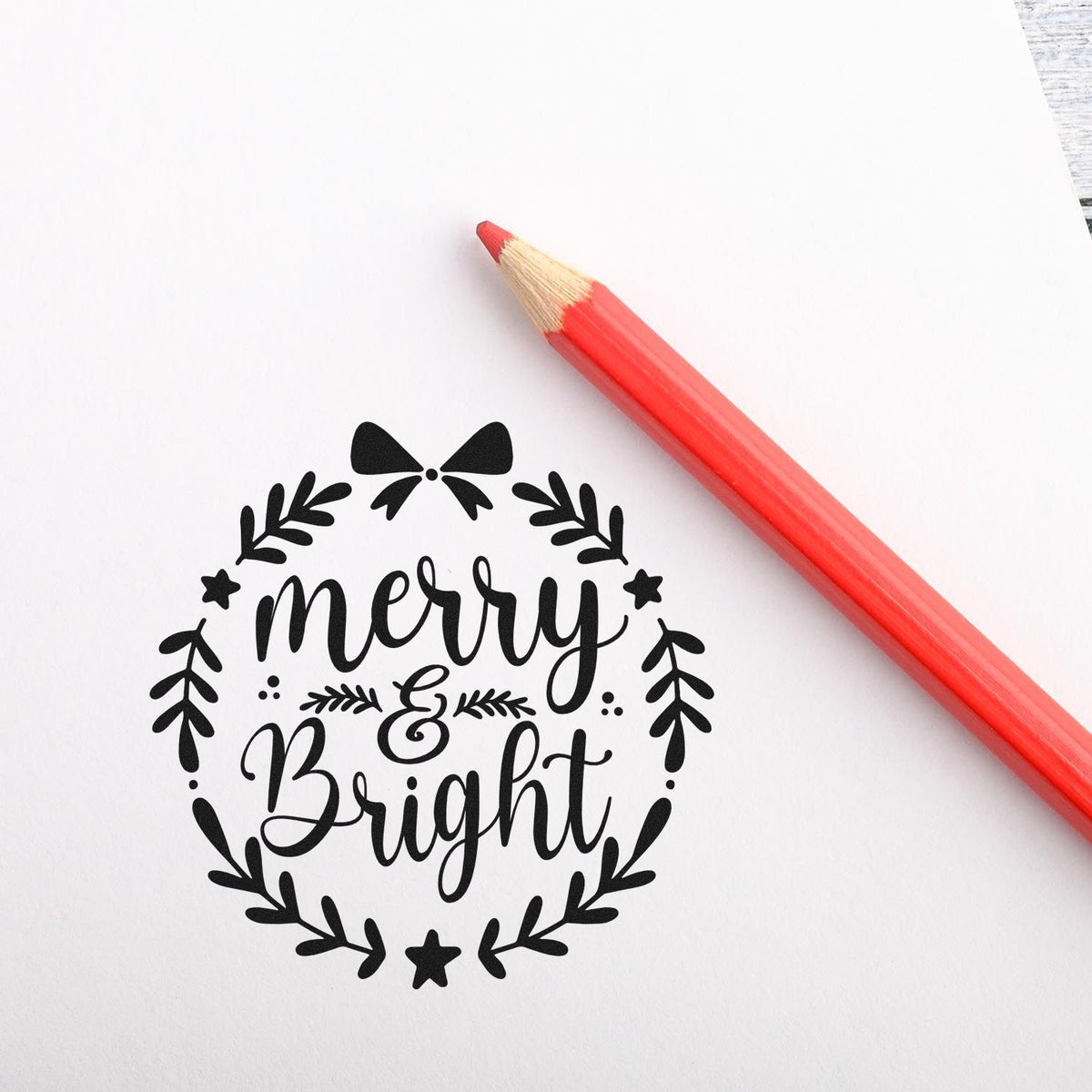 Merry & Bright holiday rubber stamp design with wreath, bow, and stars beside a red pencil on white paper.