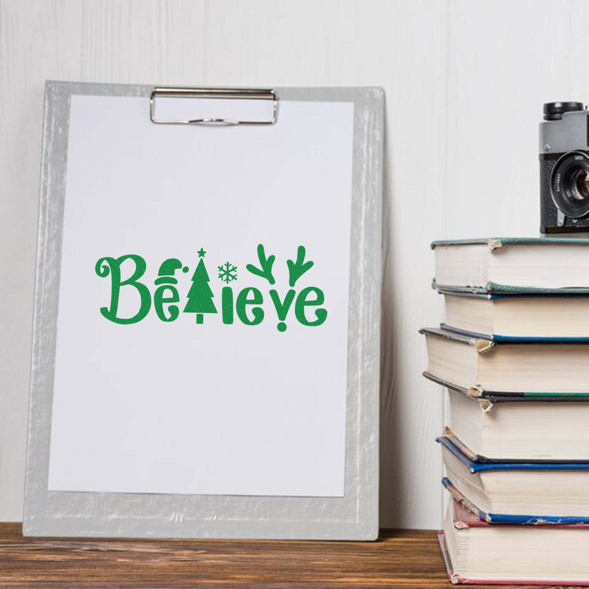 Christmas rubber stamp design featuring green Believe word art with Santa hat, tree, snowflake, and reindeer antlers.