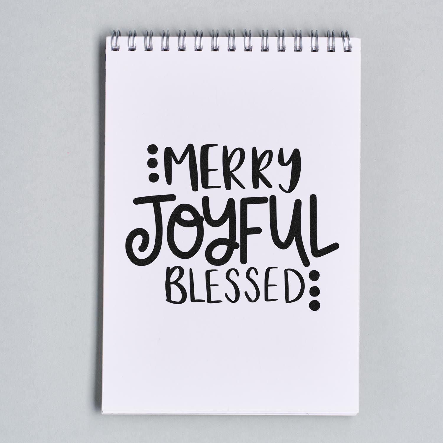 Christmas rubber stamp design reading Merry Joyful Blessed in bold hand-lettering on a notebook page.